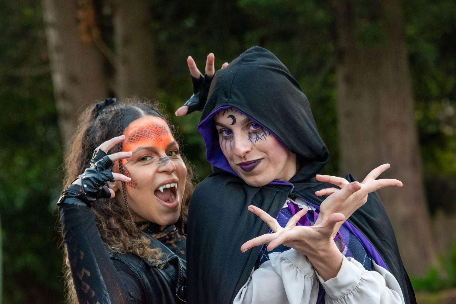 Two women in witch and sorceress Halloween costumes with dramatic makeup posing in forest.