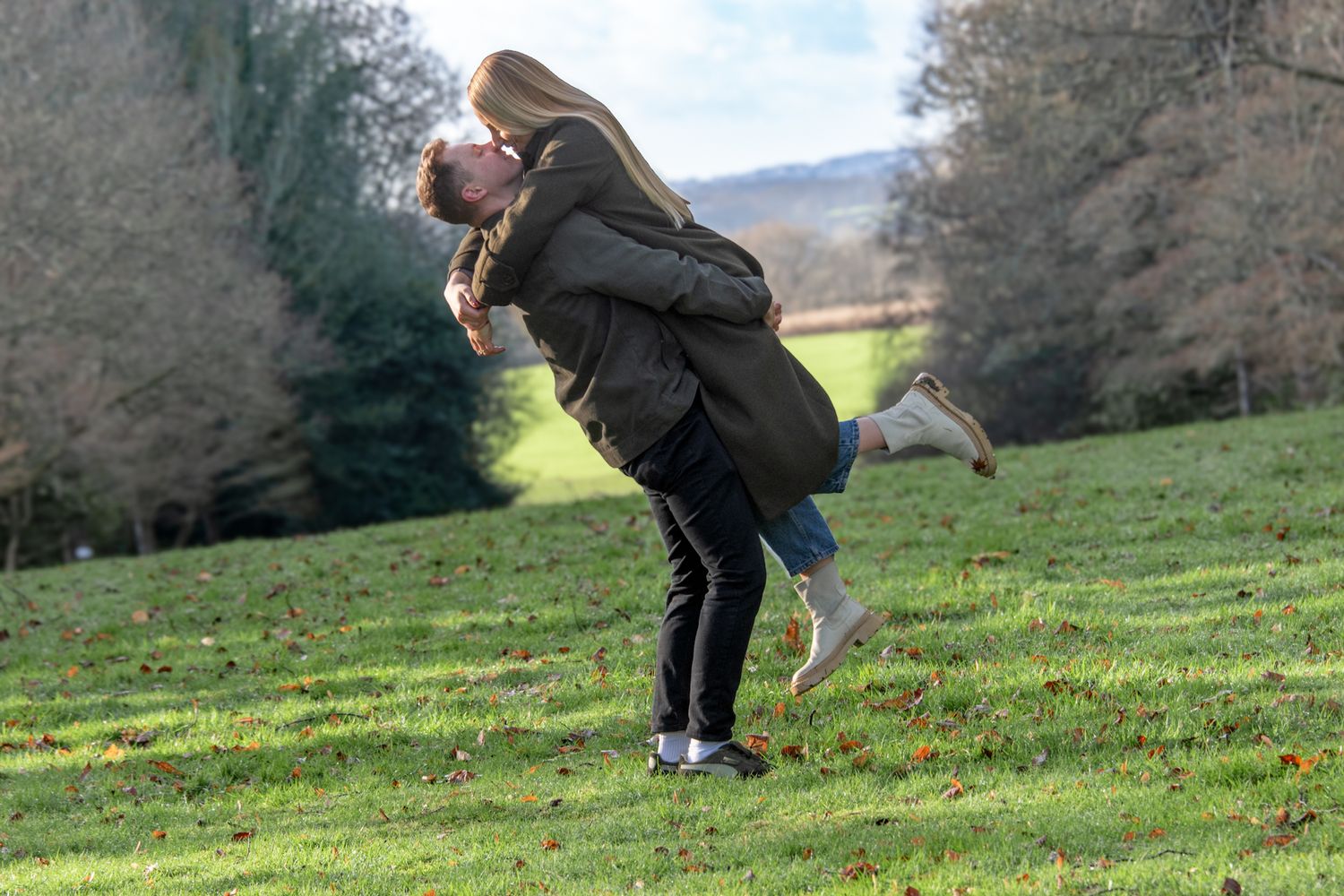 Couple playfully spinning in a green park field on a winter day.
