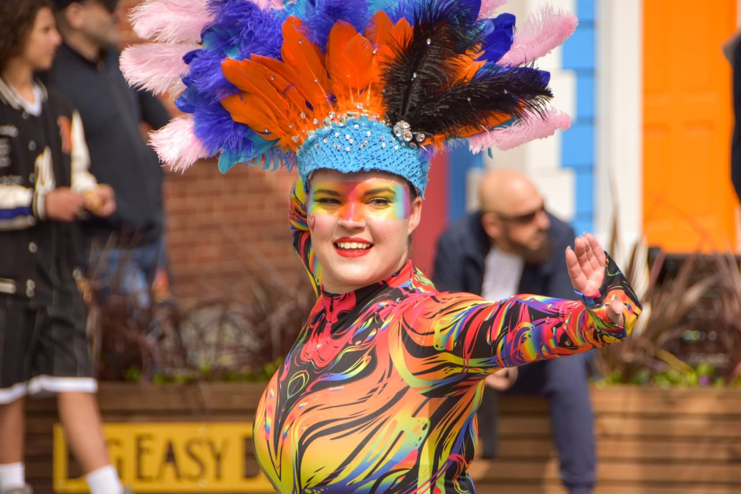 Colorful carnival dancer wearing a vibrant feathered headdress and painted bodysuit performing at a festival.