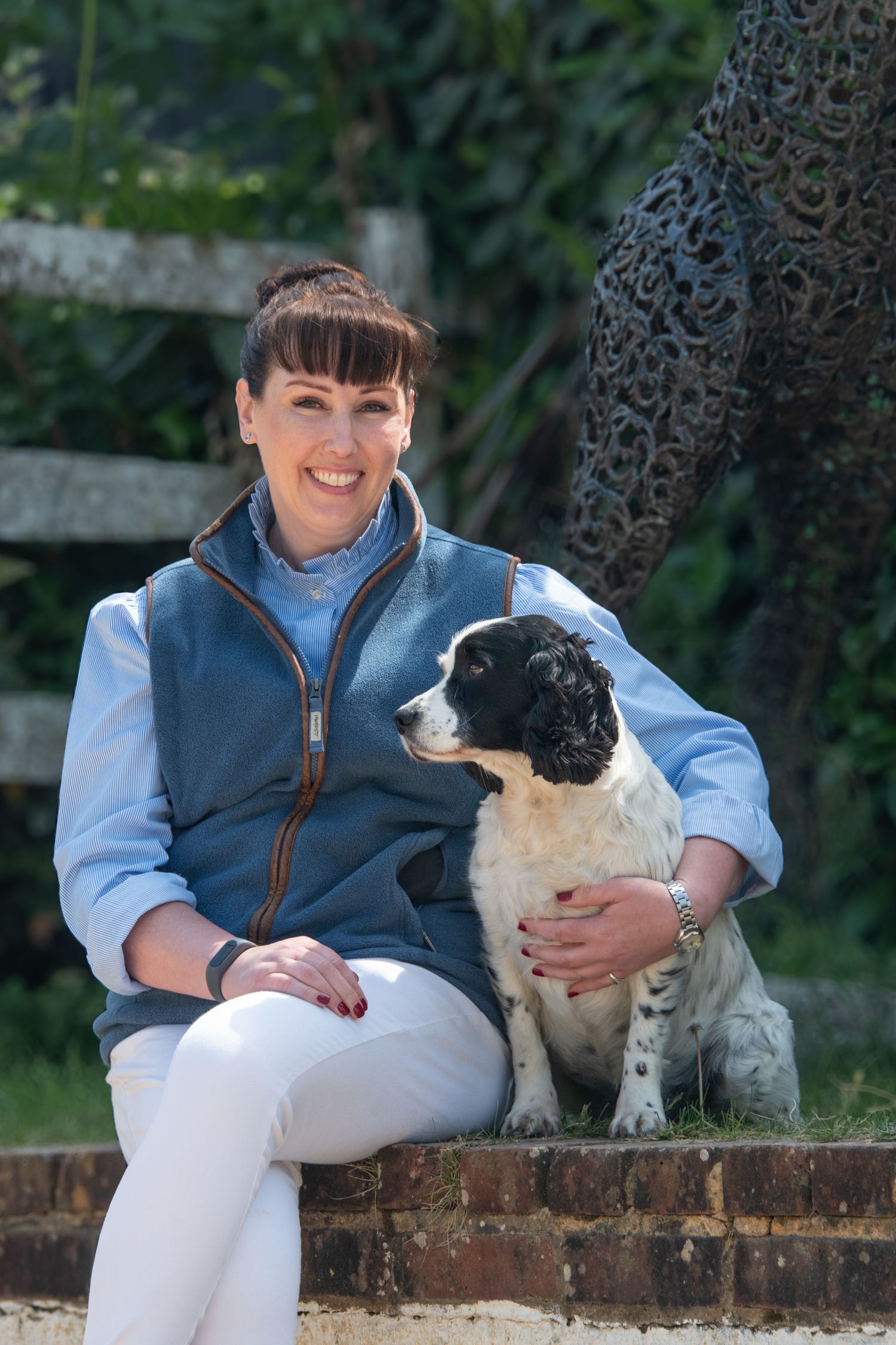 Smiling dark-haired woman in a blue vest sitting with a black and white Springer Spaniel.