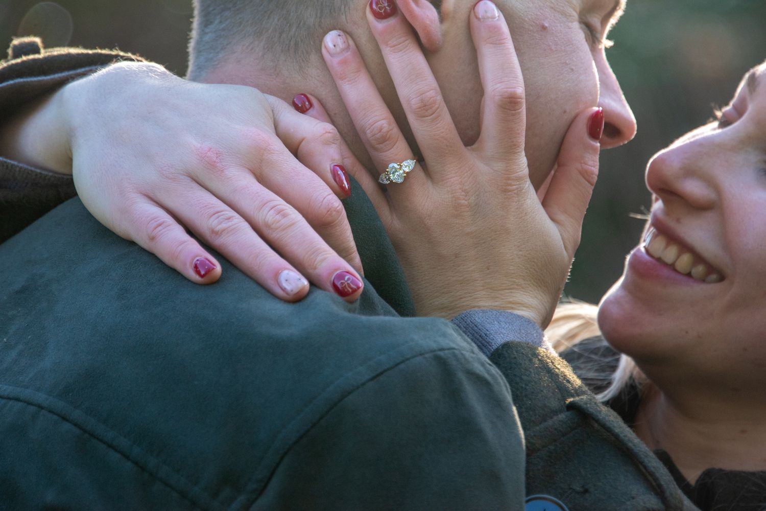 Close-up of smiling woman showing diamond engagement ring while hugging partner outdoors.