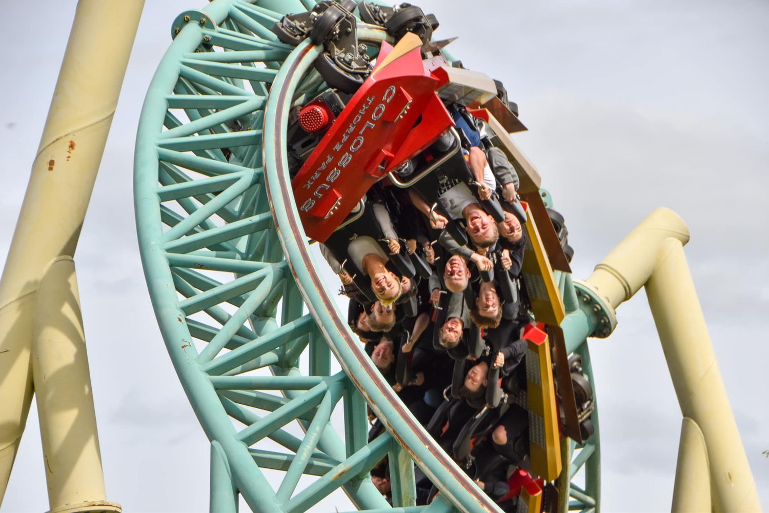 Thrill-seekers riding a green and red roller coaster through a steep curve at an amusement park.
