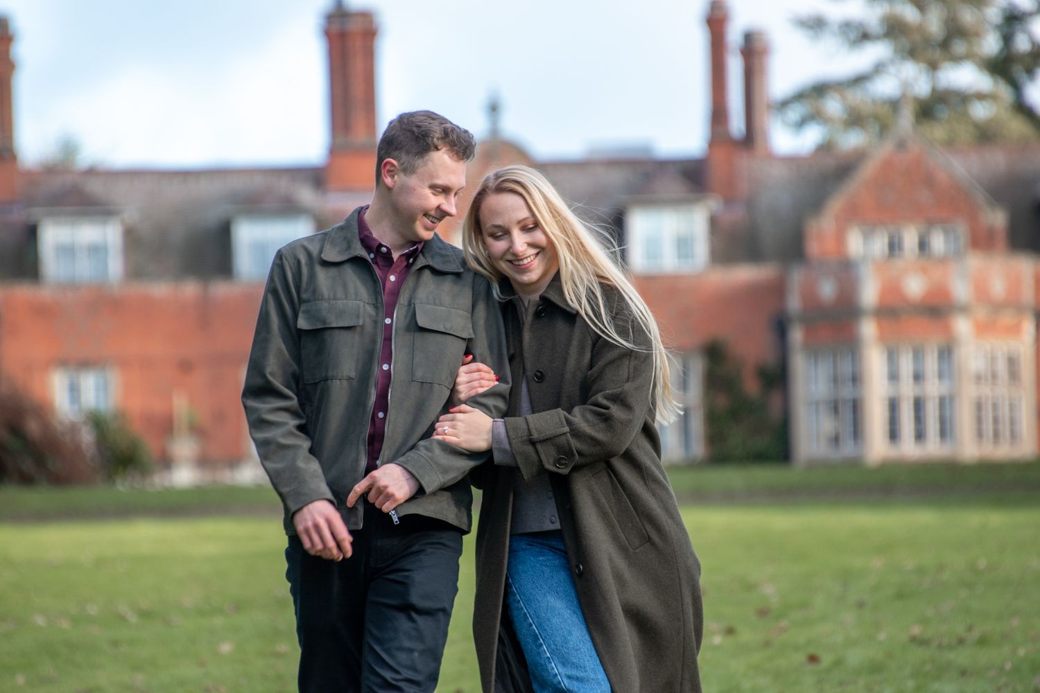Happy engaged couple walking and laughing together on the grounds of a red brick country manor.
