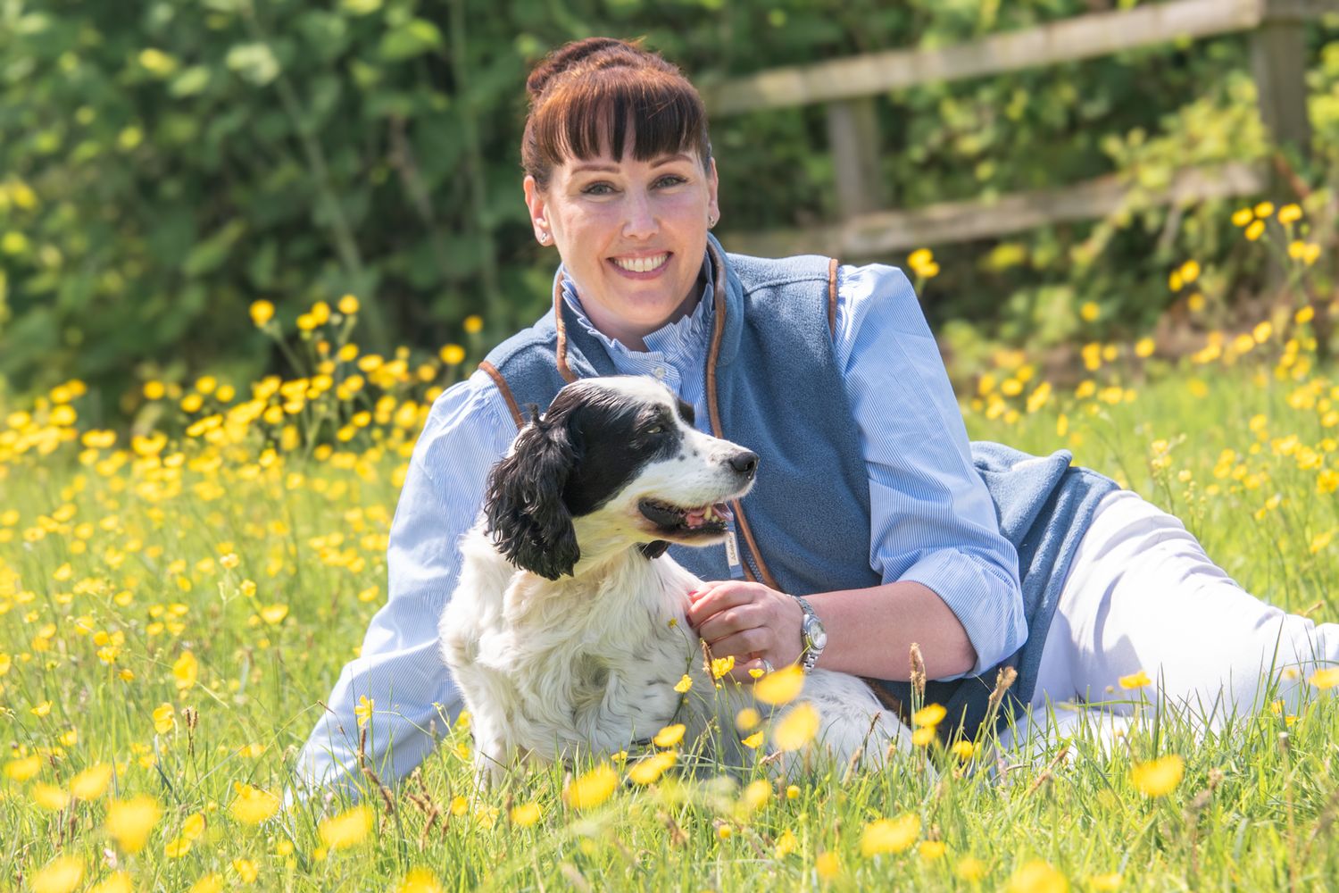 Woman smiling with black and white Springer Spaniel dog in a sunny meadow filled with yellow buttercups.