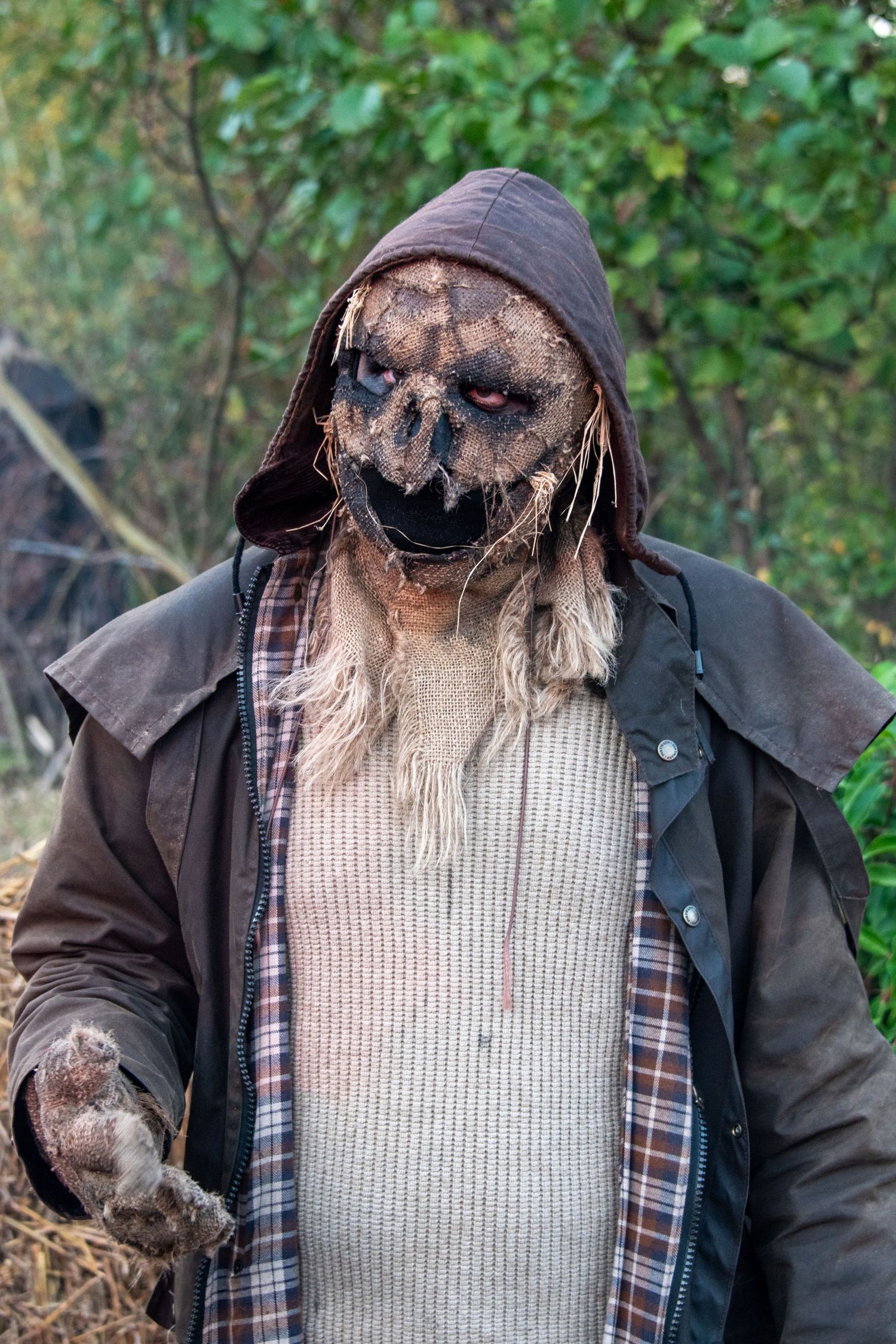 Frightening scarecrow monster costume with dark mask and tattered clothing in outdoor setting.