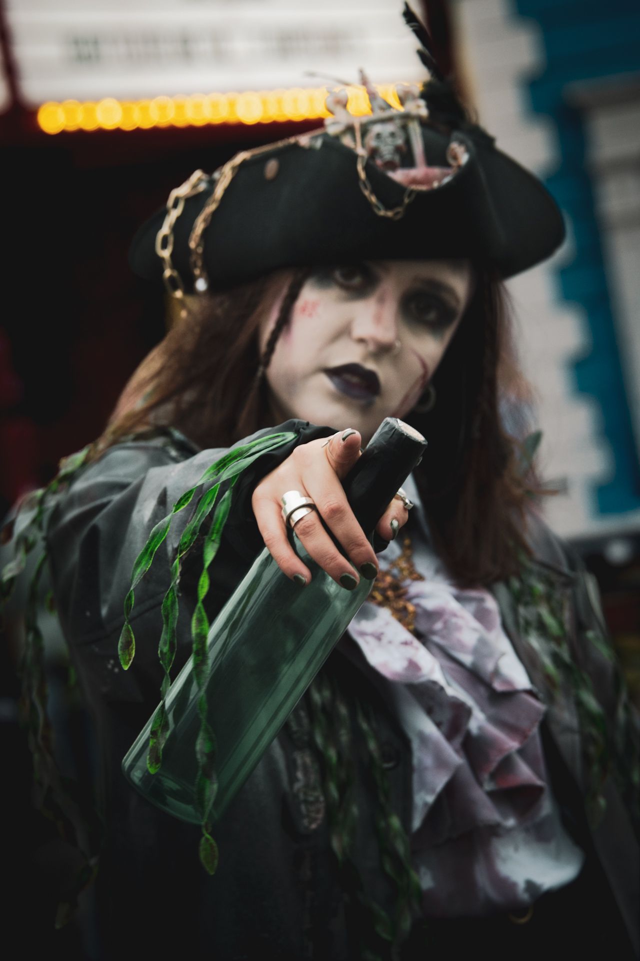 Woman in elaborate zombie pirate Halloween costume pointing a dagger toward camera at a fairground attraction.