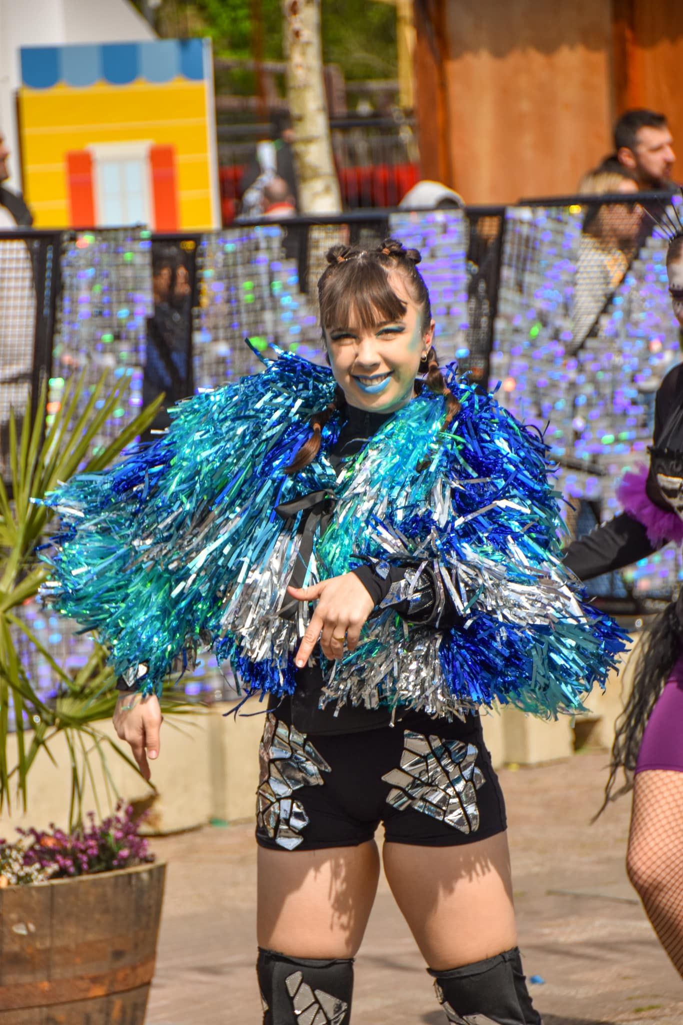 Smiling festival dancer in blue and silver tinsel costume posing at an outdoor carnival event.