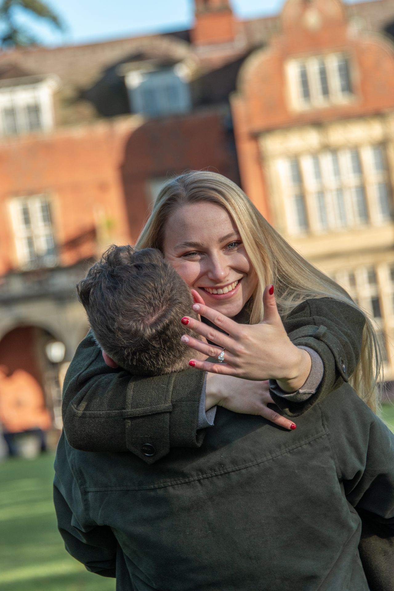 Joyful woman hugging her fiance outdoors, showing her diamond engagement ring while smiling broadly.