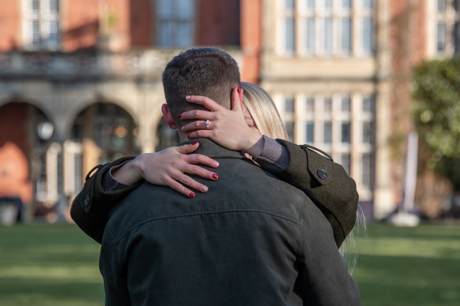 Couple sharing tender embrace outside historic brick building after engagement proposal.