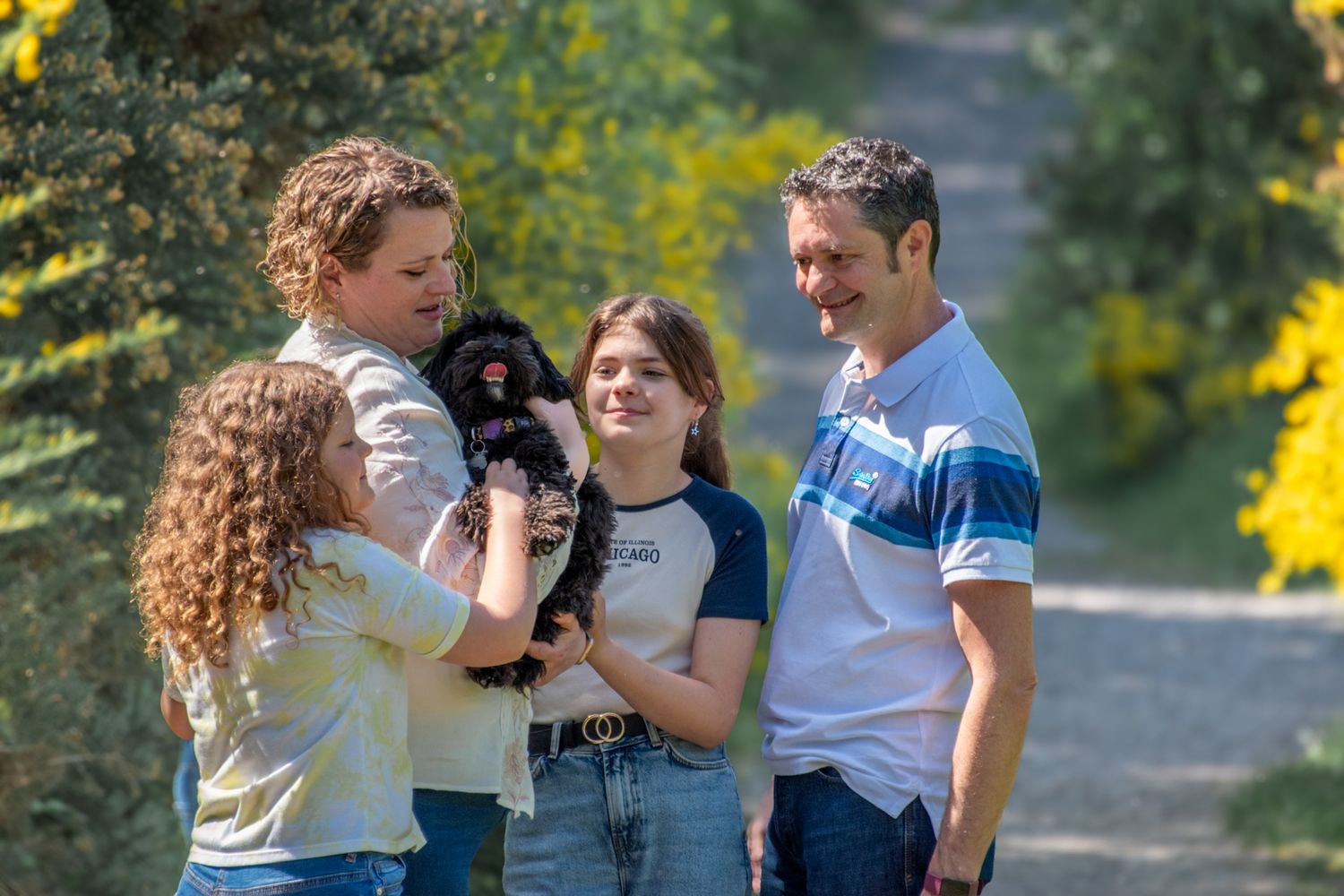 Happy family of four admiring a small black puppy outdoors in sunny garden setting.