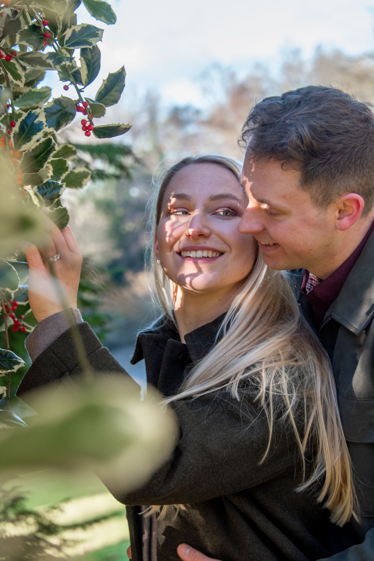 Happy couple smiling together near holly berries in a sunlit garden.