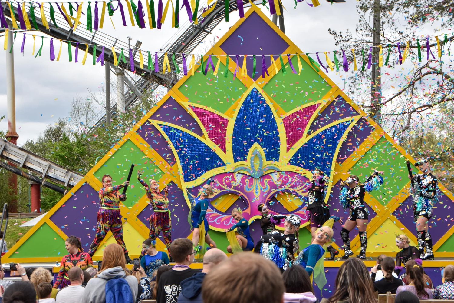 Vibrant Mardi Gras stage show with dancers in colorful costumes performing before a large decorative backdrop.