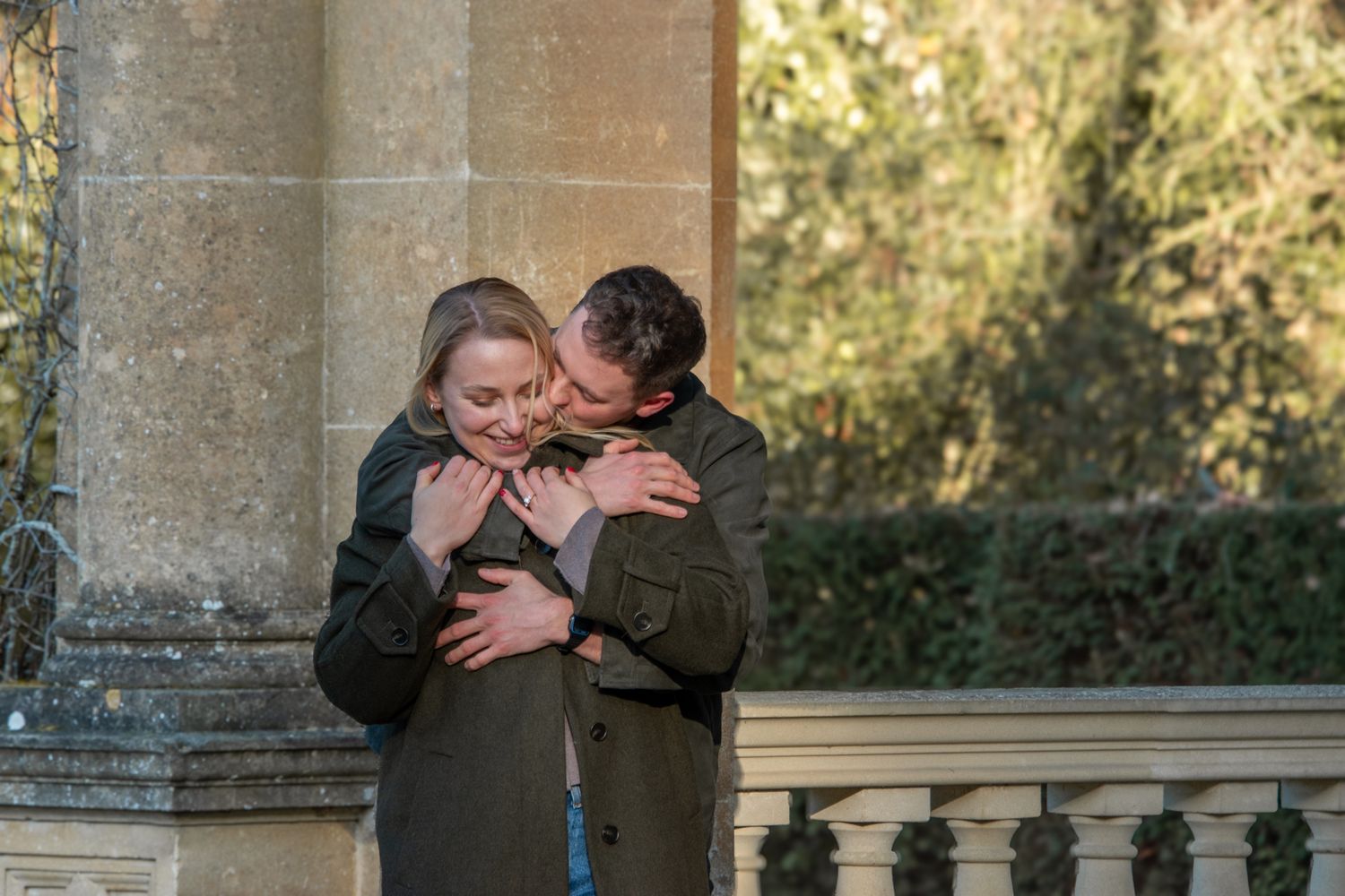 Couple embracing and kissing near stone columns in a garden setting.