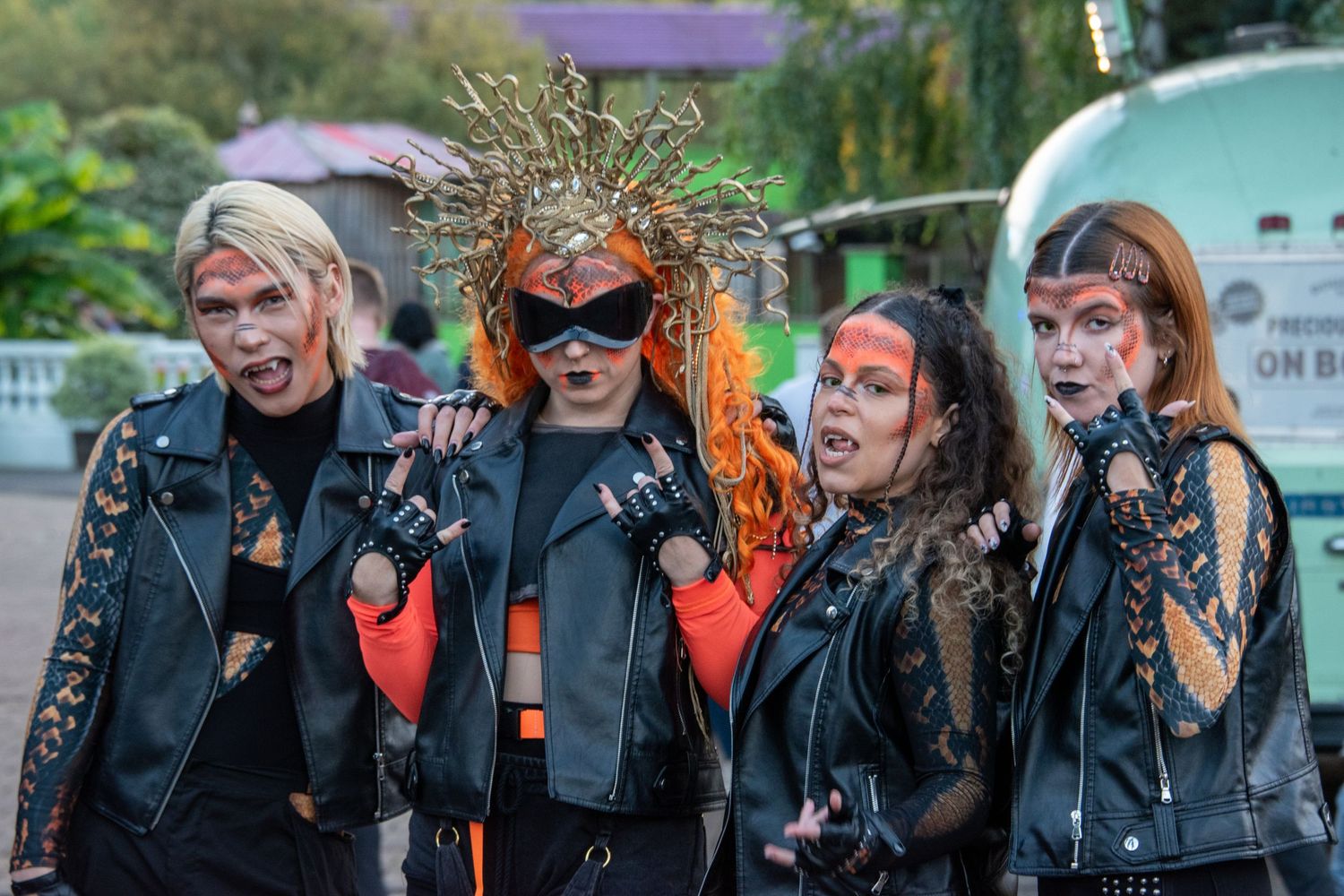 Four people in Halloween costumes with dark makeup and leather jackets pose together outdoors.