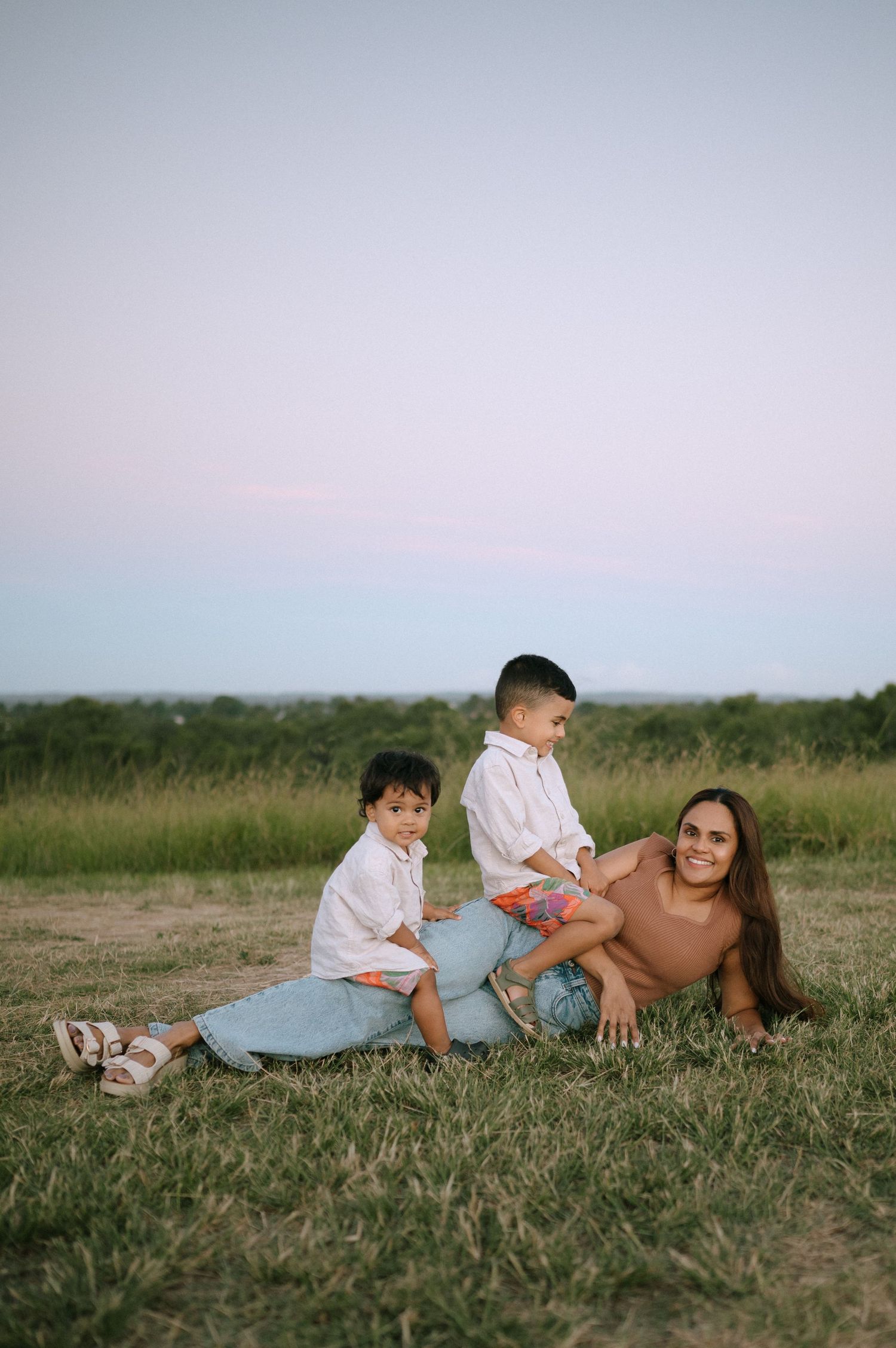 A family shares a playful moment together while lying in a grassy field on a sunny day.
