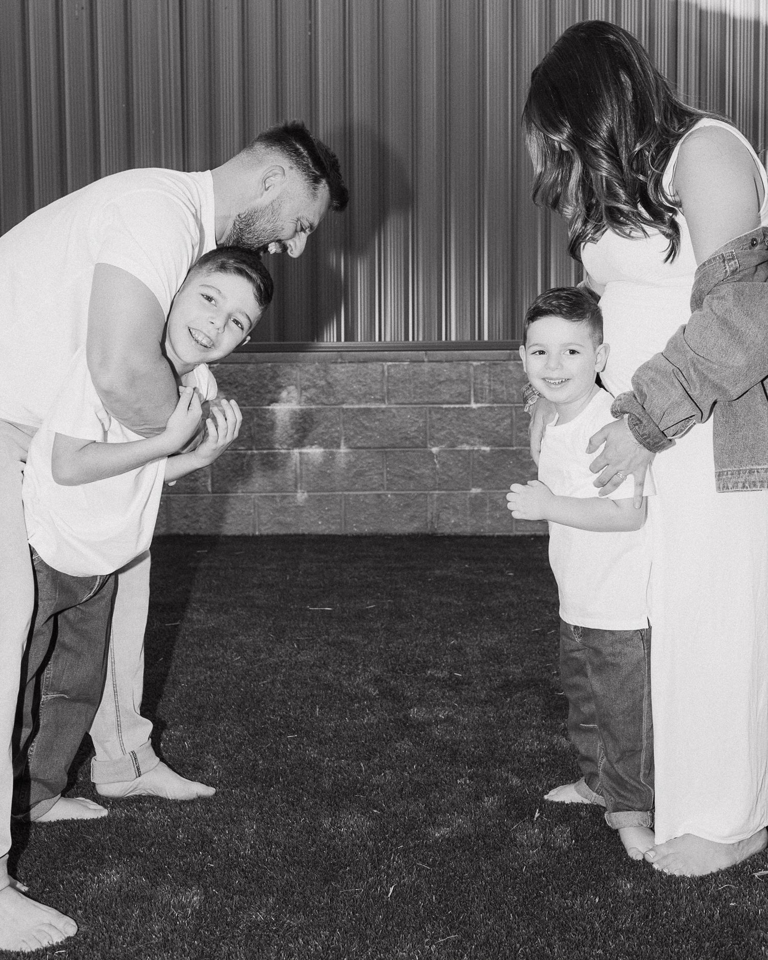 Family members playing and laughing together on grass in black and white.