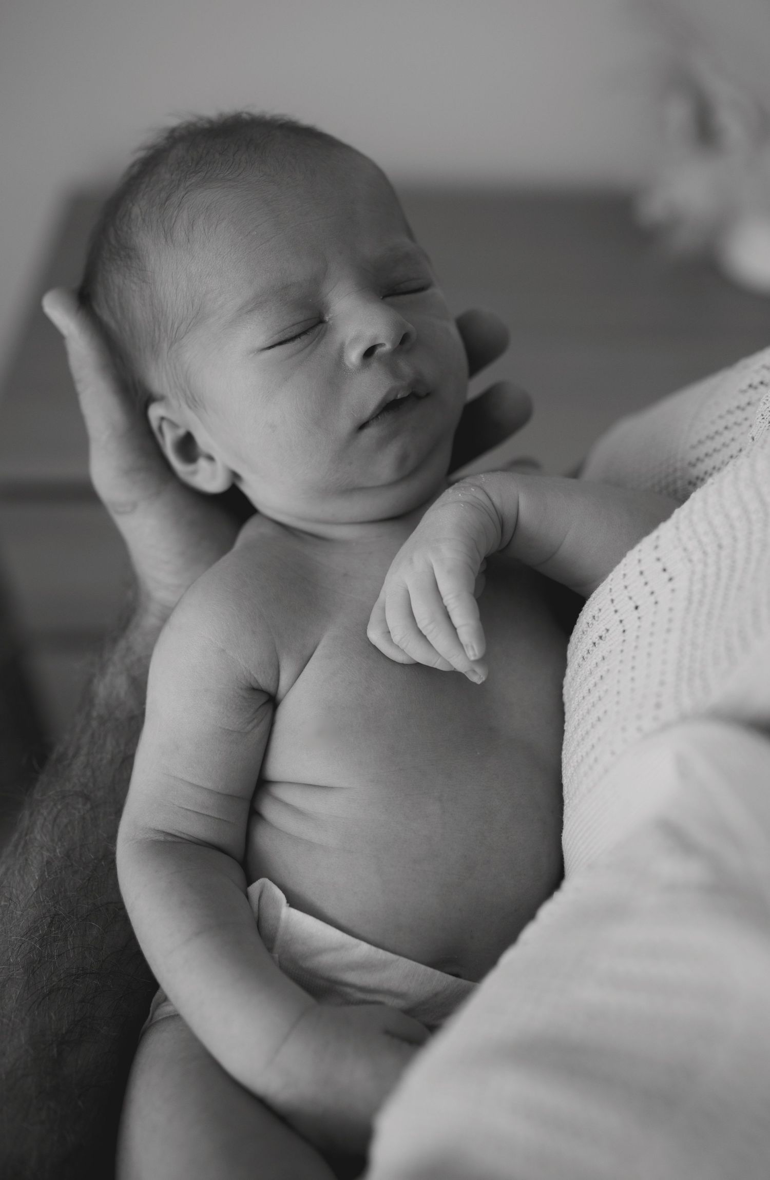 Black and white photo of a sleeping newborn baby cradled gently in an adult's hands.