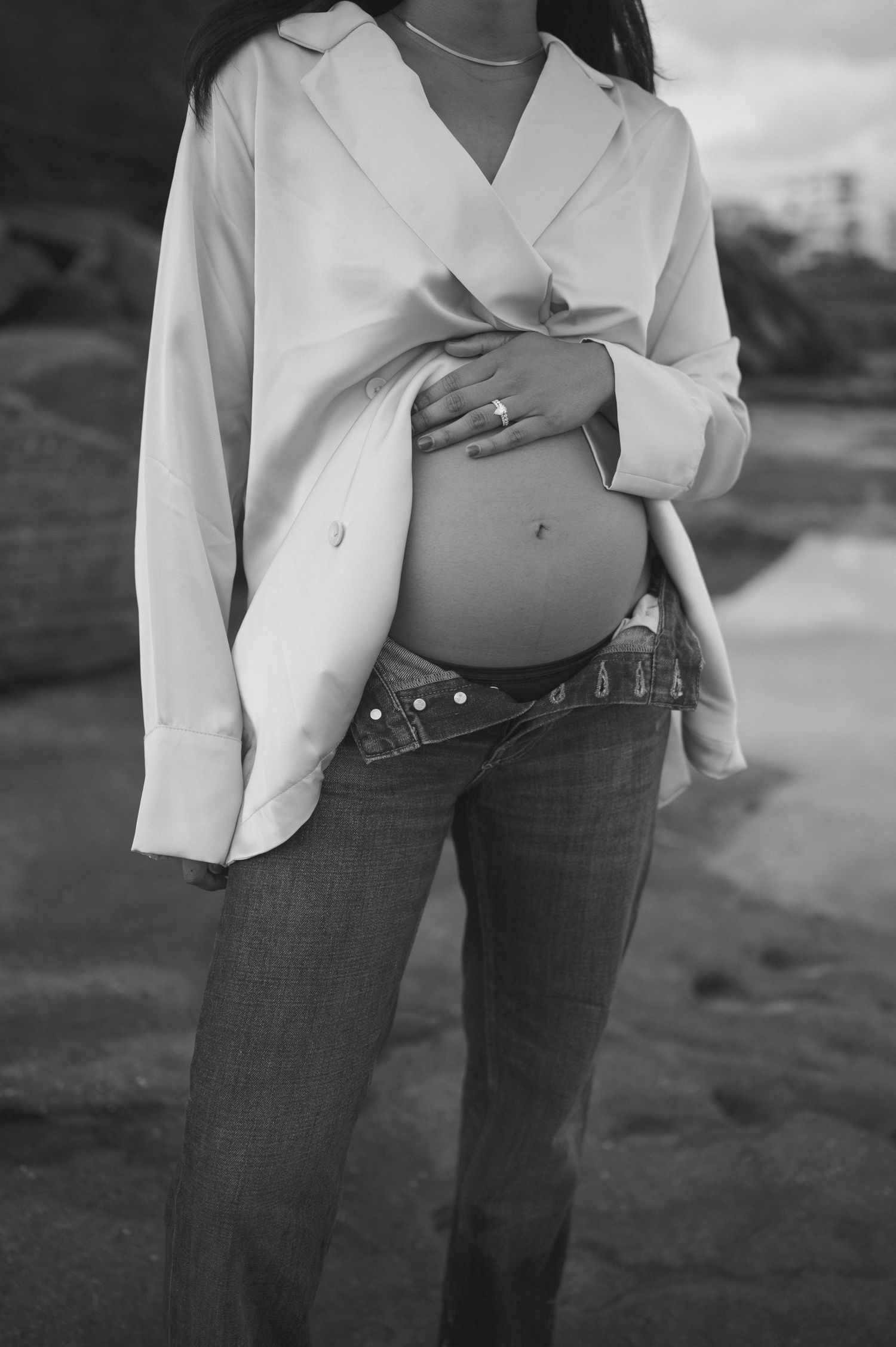 Artistic black and white maternity photos featuring white shirt and jeans on beach.