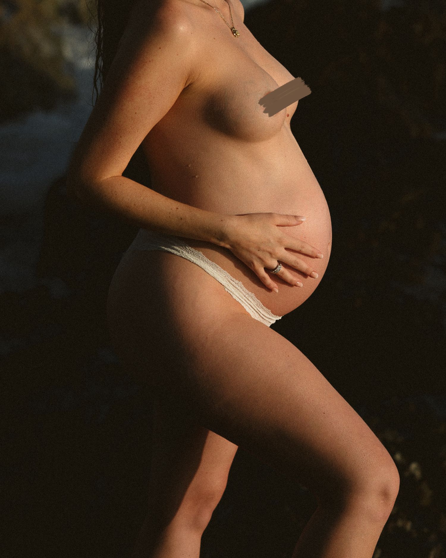 Artistic maternity photo with dramatic lighting highlighting pregnant belly against dark background.