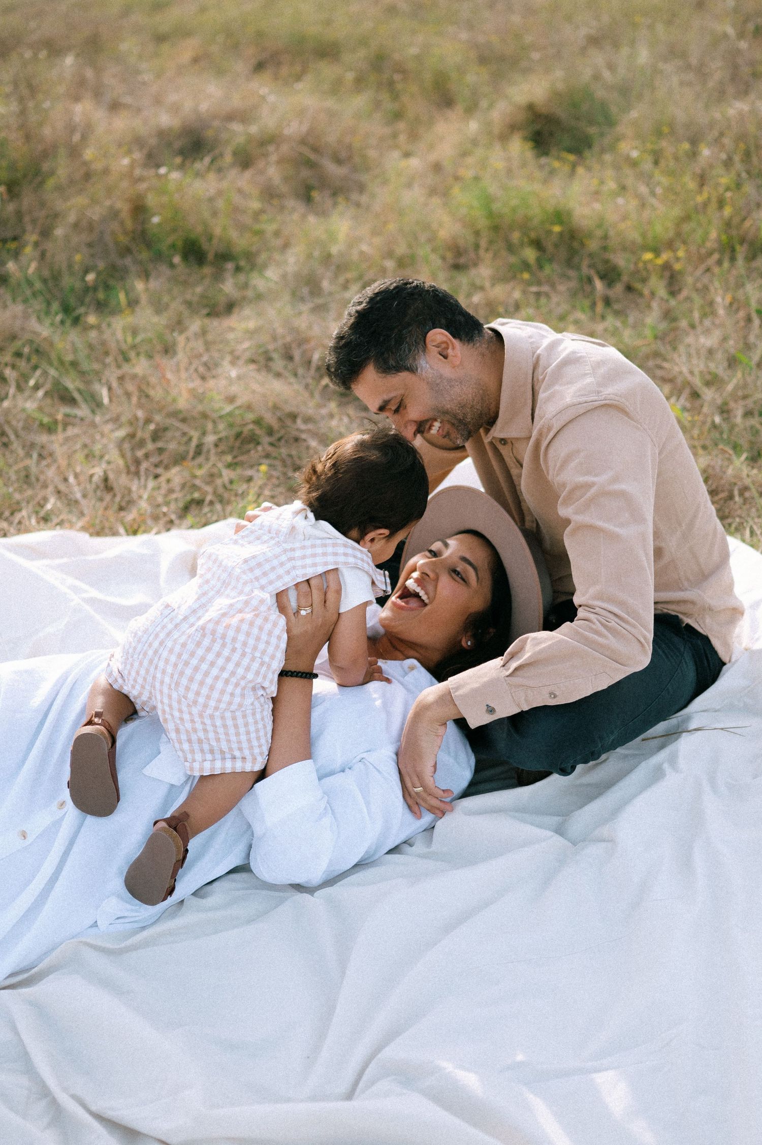 Family sharing joyful moment while lying on white blanket in grassy field.