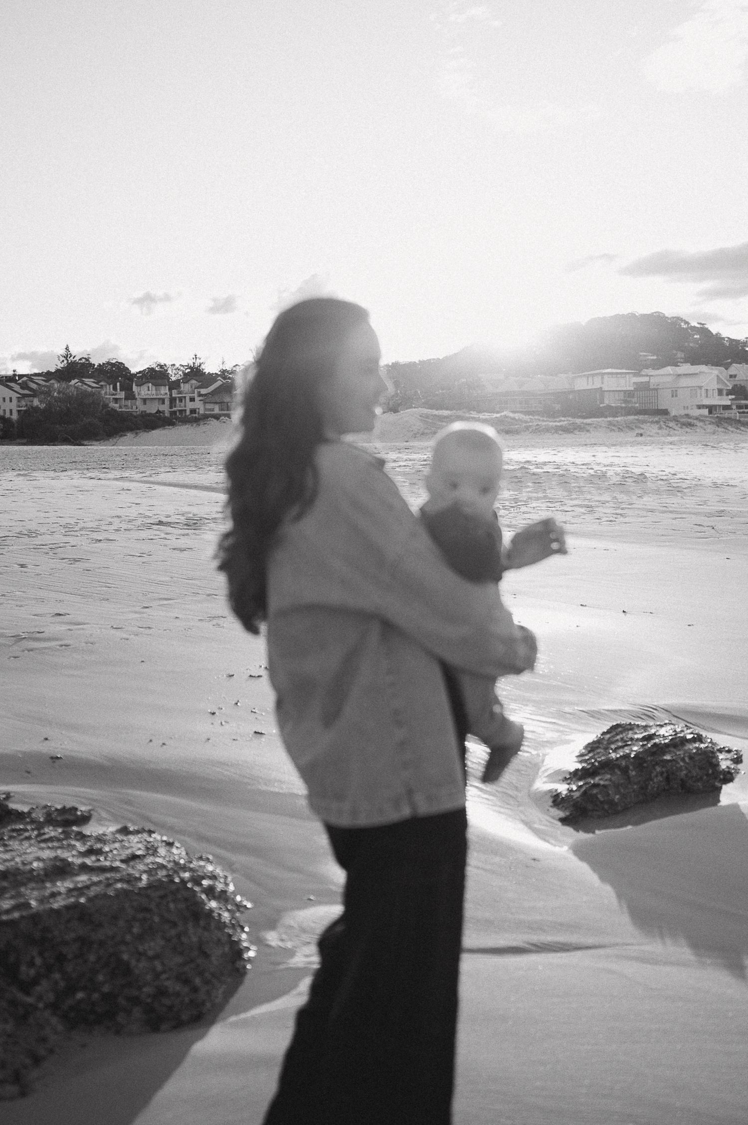 Silhouettes against sunset on beach with waves and rocks in background.