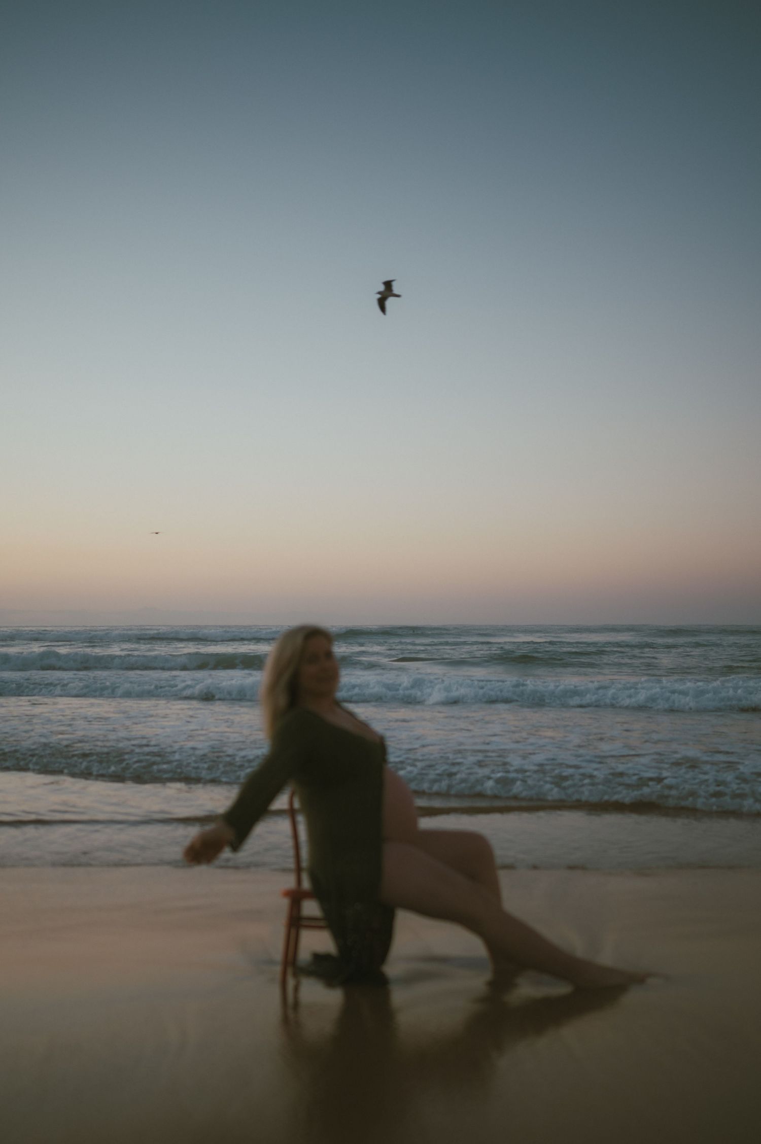 Silhouetted figures on beach at sunset with waves and seabirds in background.