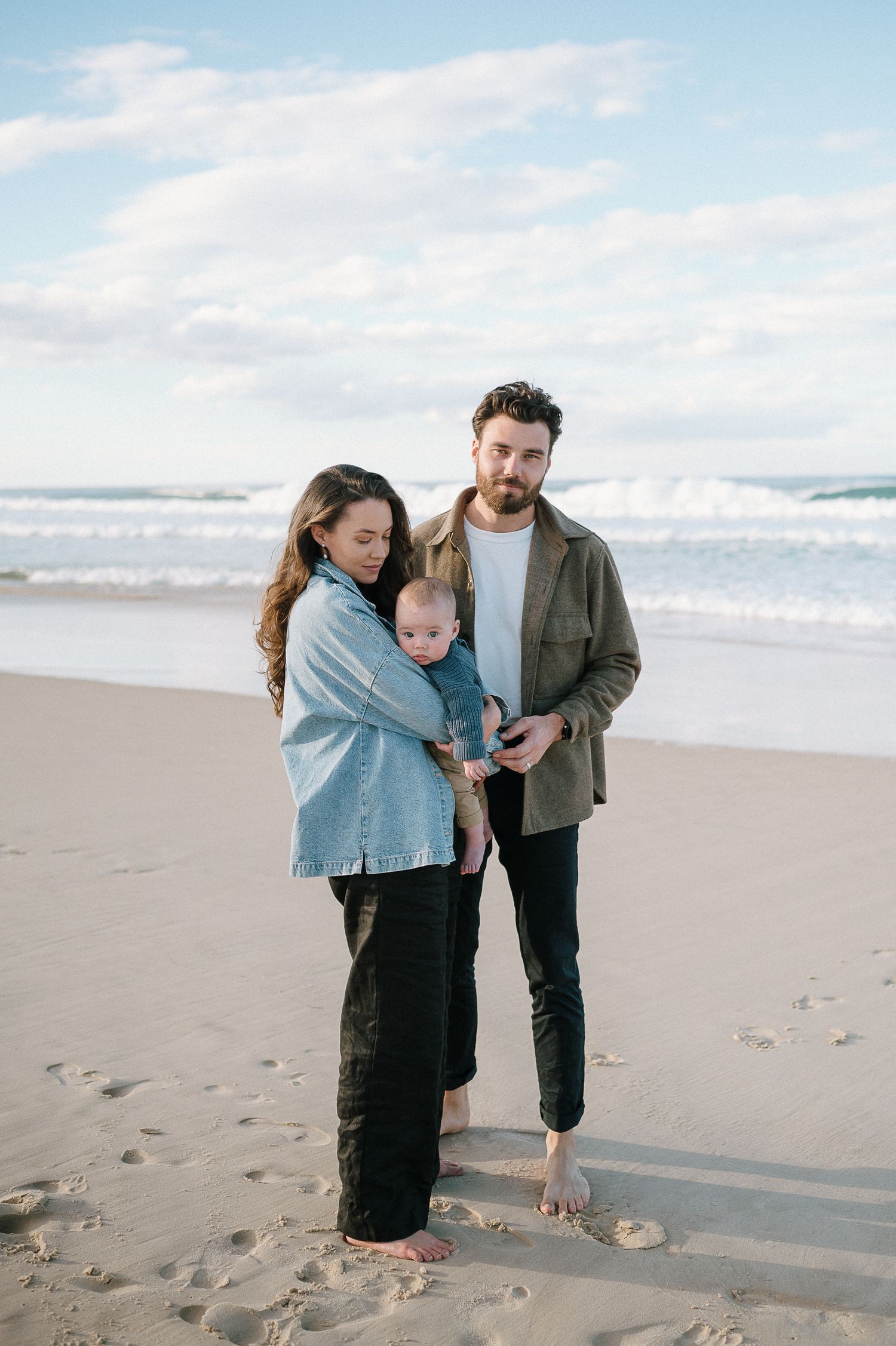 Family enjoying a peaceful moment together on a sandy beach with ocean waves in the background.