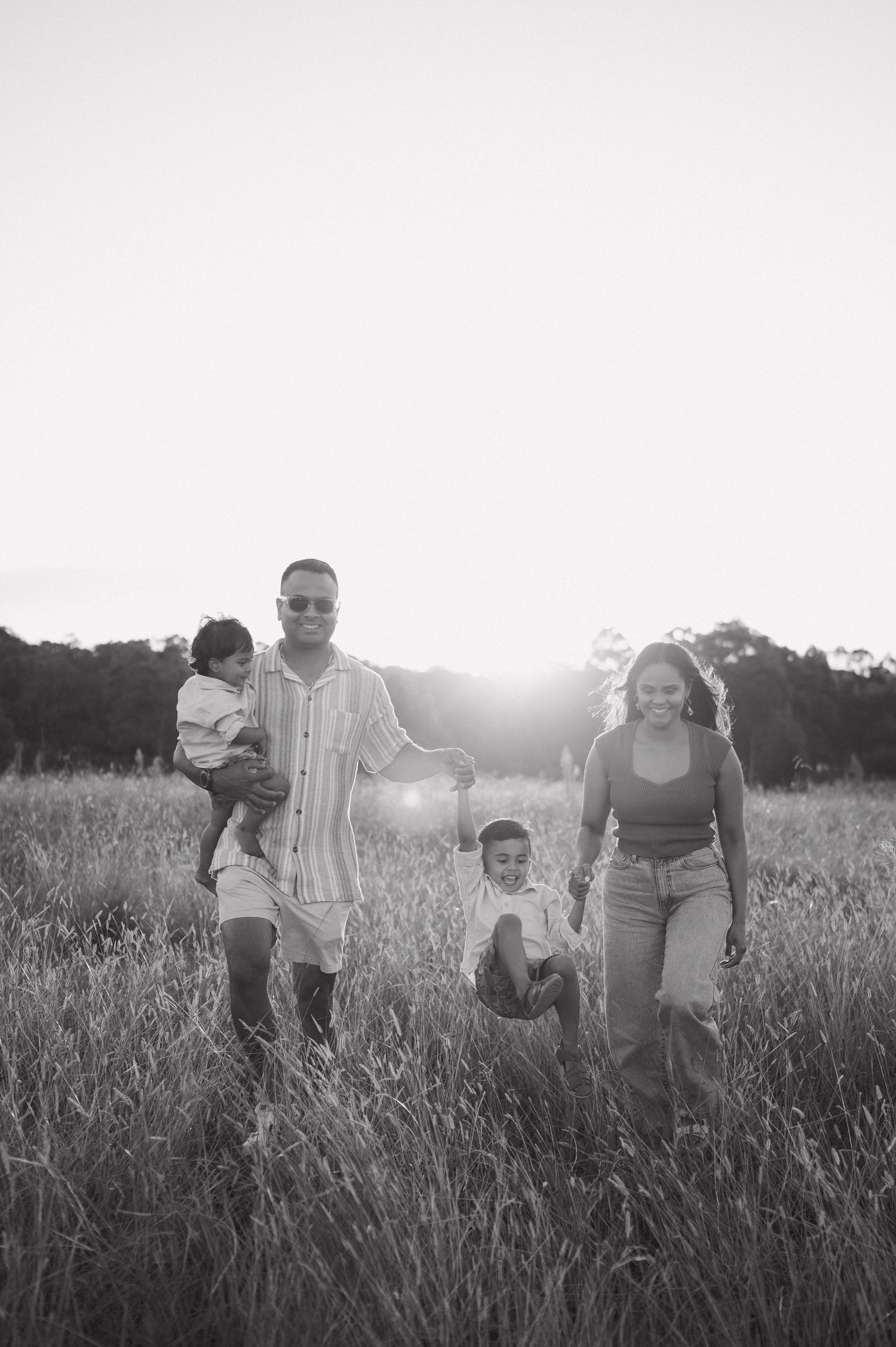 Black and white photo of family walking through tall grass at sunset.