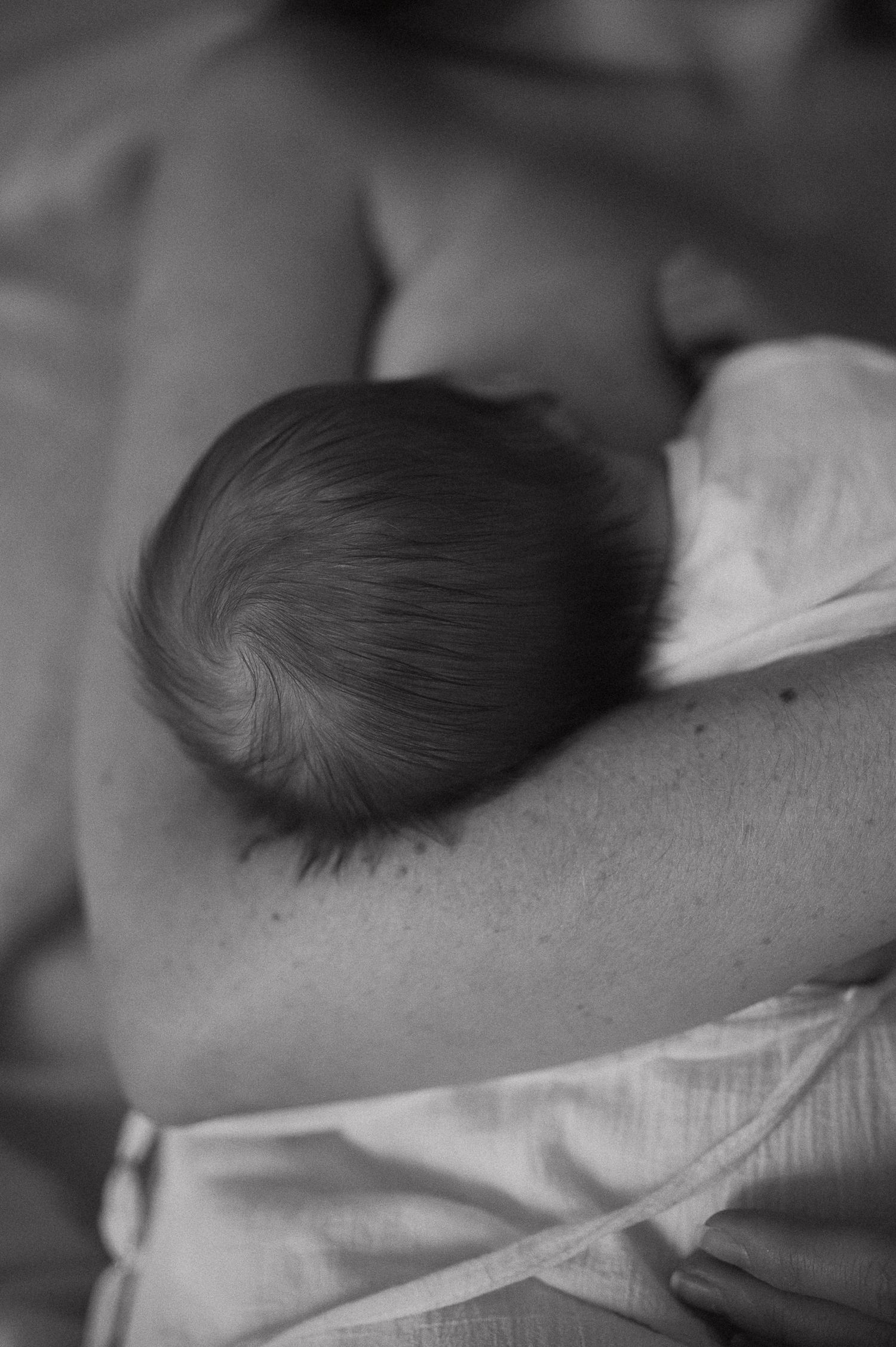 Black and white photo of a newborn baby breastfeeding, cradled in mother's arms.