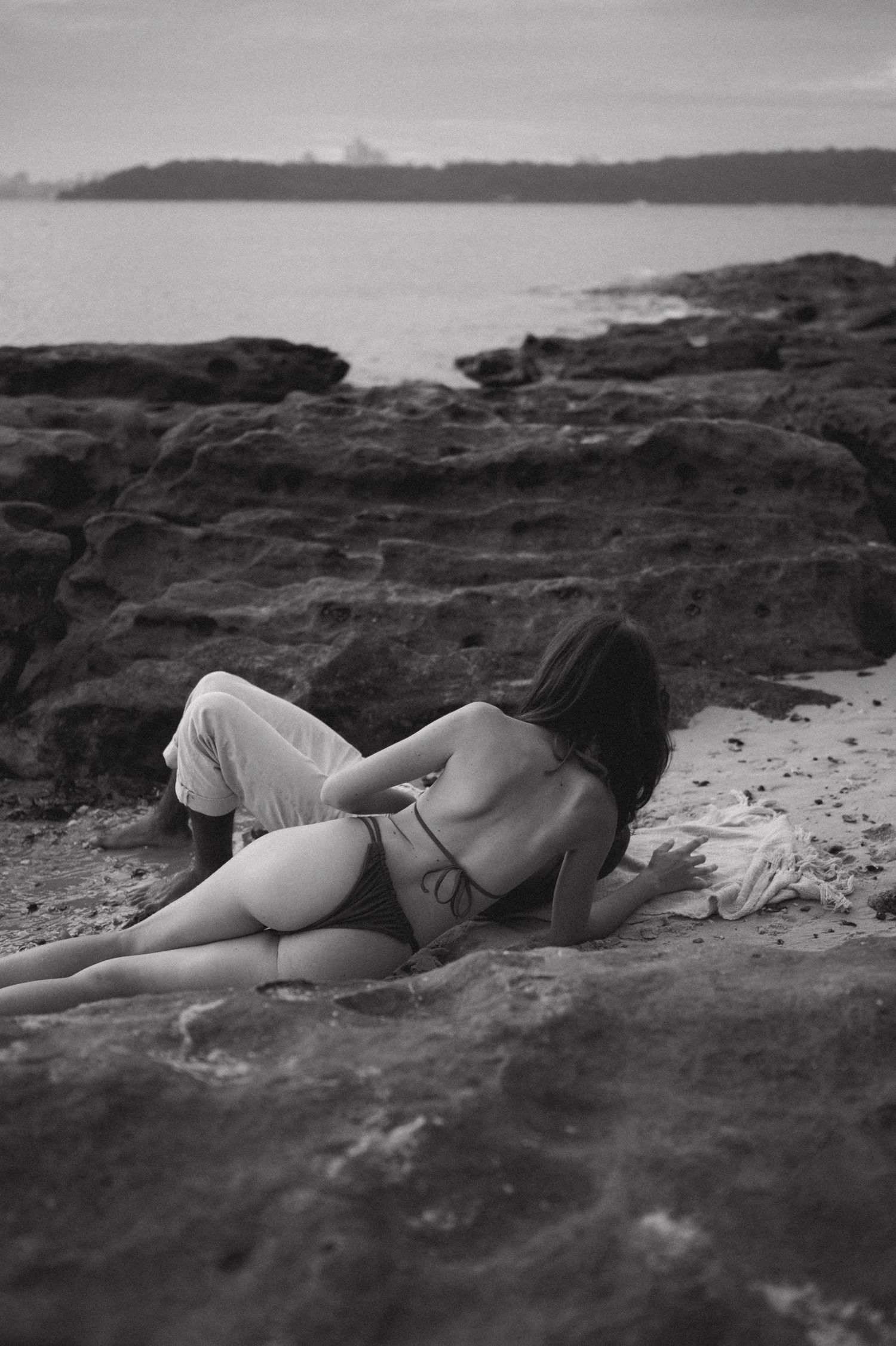 A person rests peacefully on rocky coastal terrain in black and white.