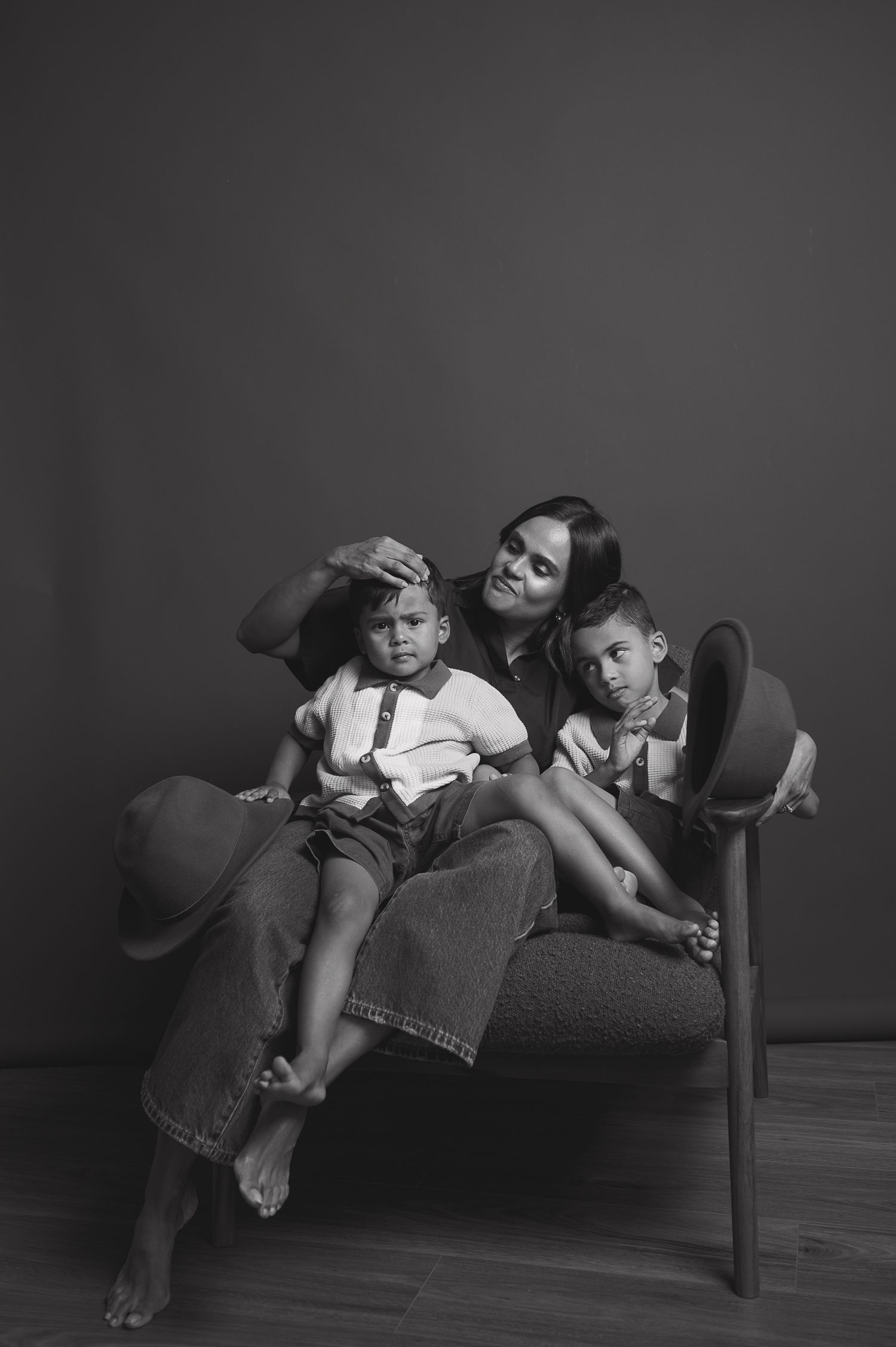Black and white portrait of a mother sitting on a chair with her two young sons in a studio setting.