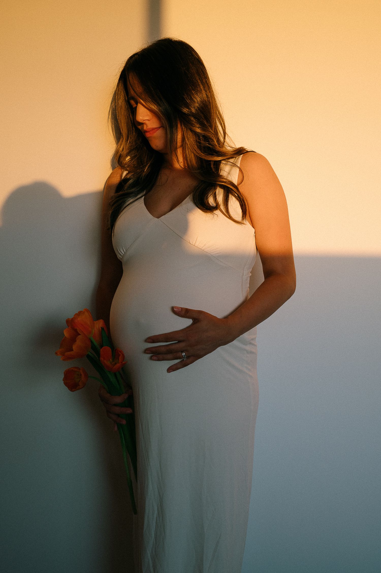 Artistic portrait of woman in white dress against orange sunset backdrop.
