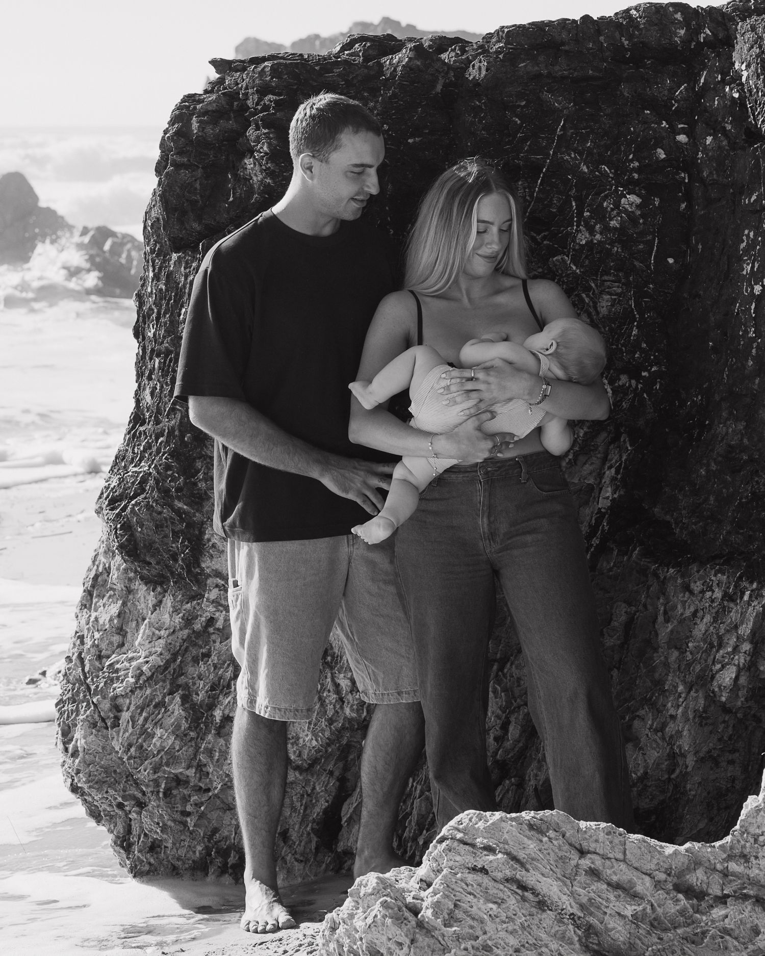 A family shares tender moments together near rocky coastal cliffs by the ocean.