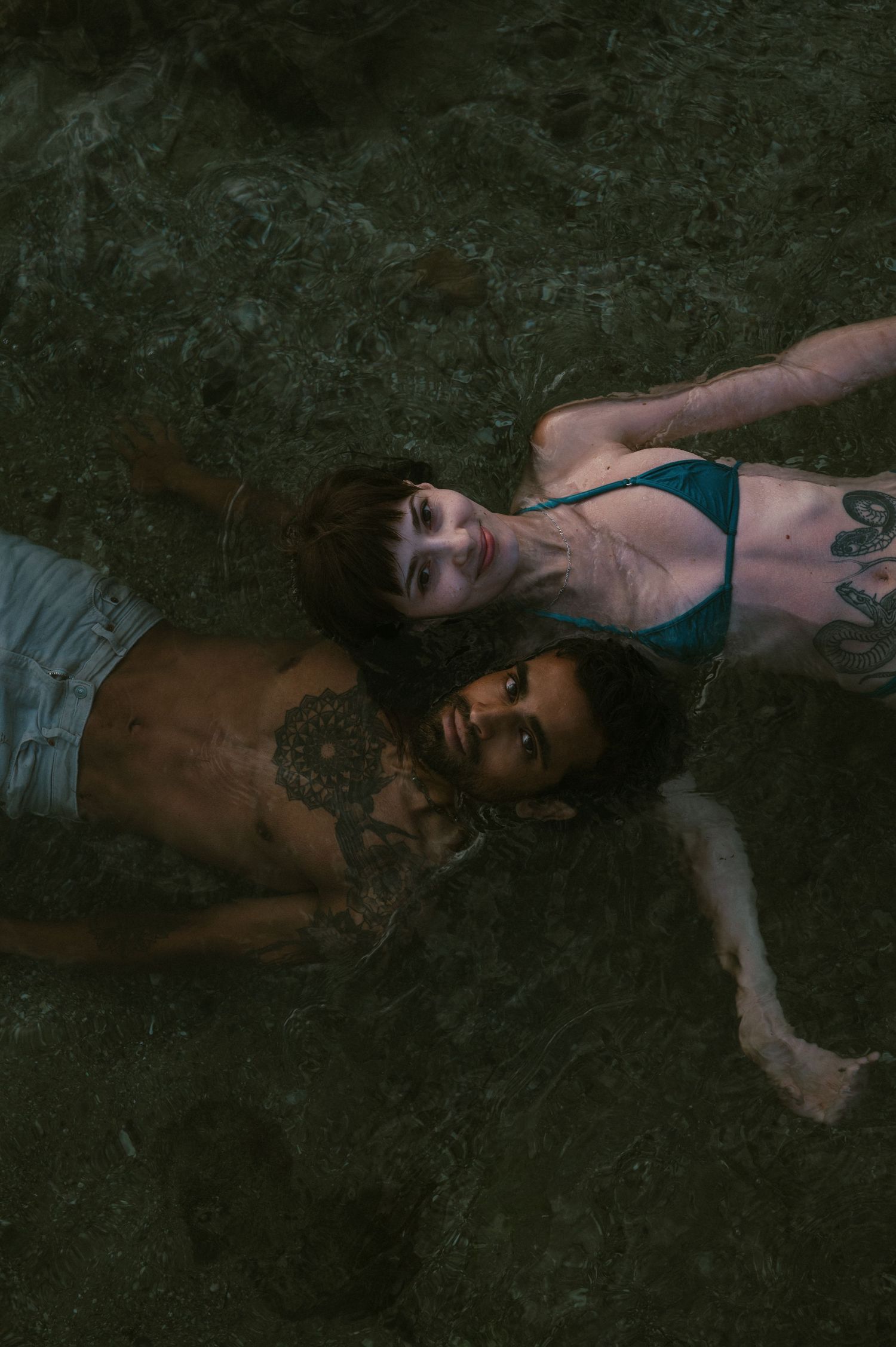 Two people lie close together on dark rocks near water.