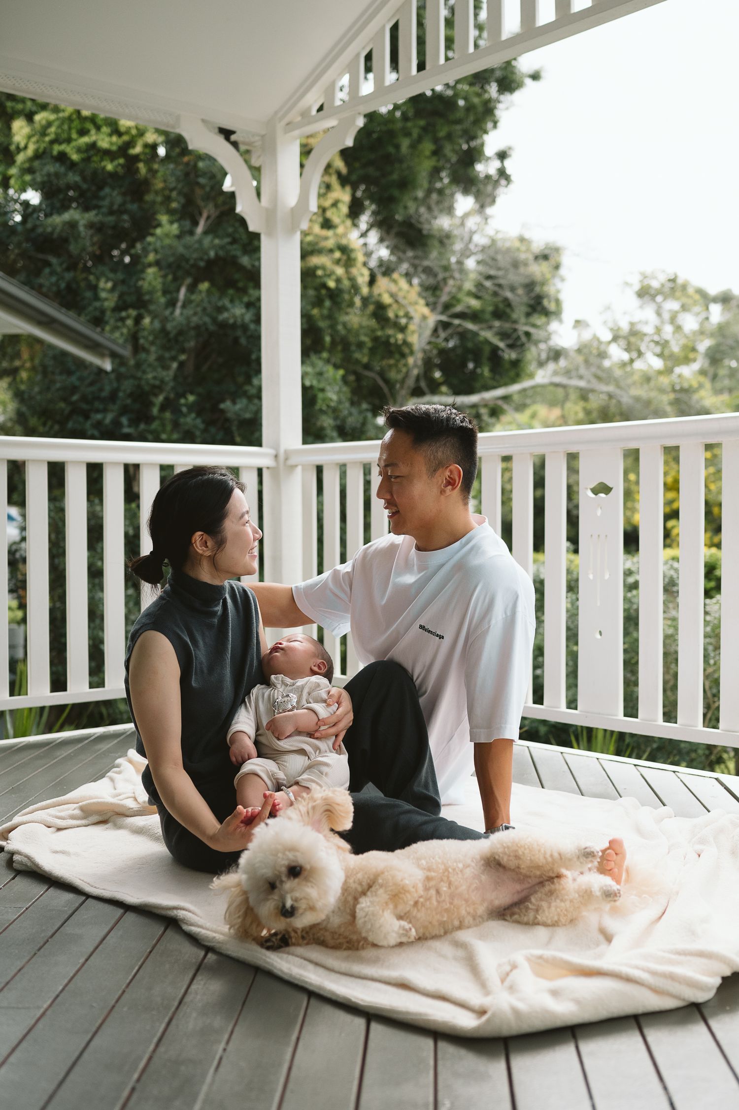 Family relaxing on a white porch with their fluffy dog and baby.