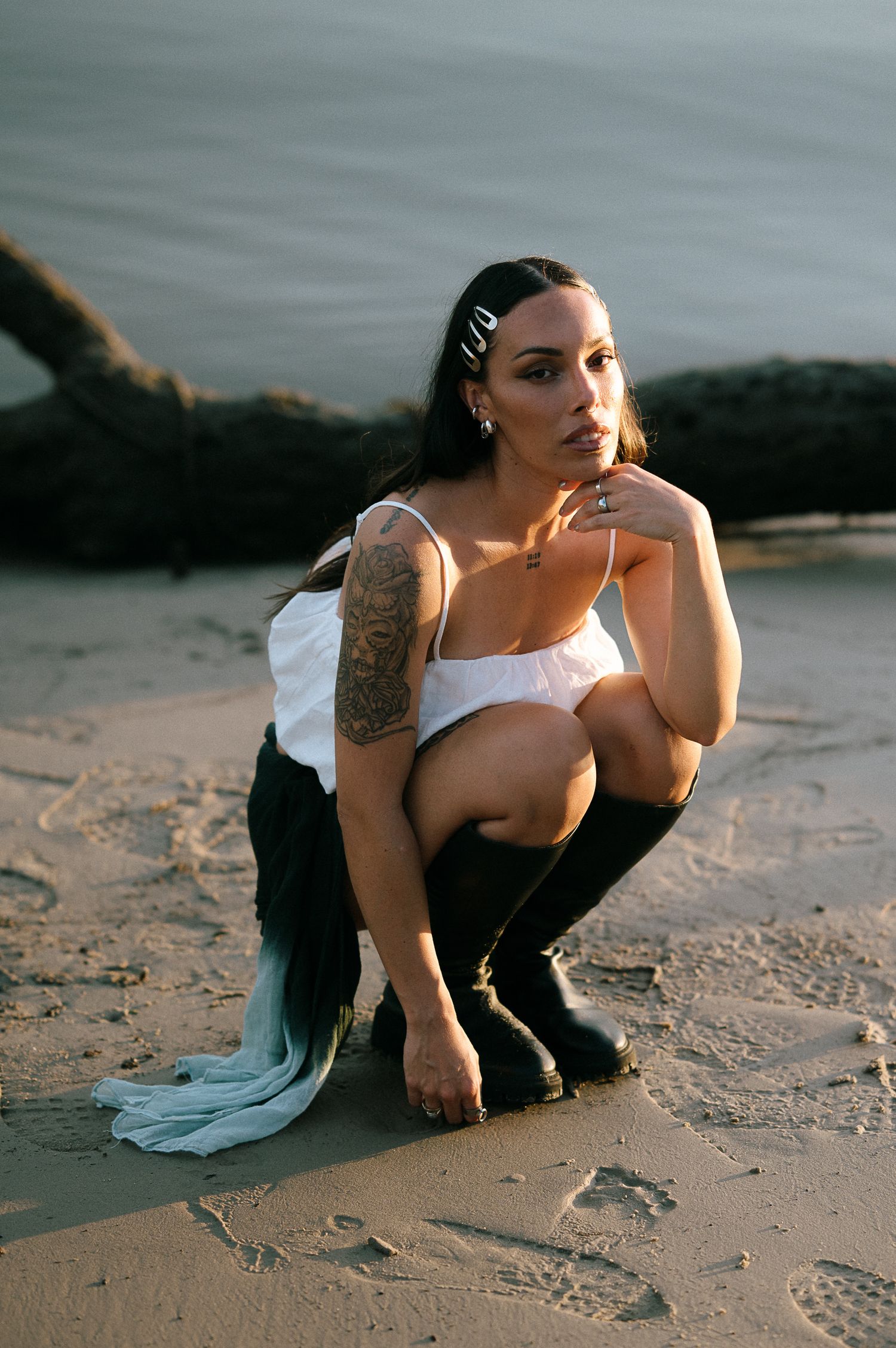 Artistic portrait at sunset on a beach with black boots and white dress.