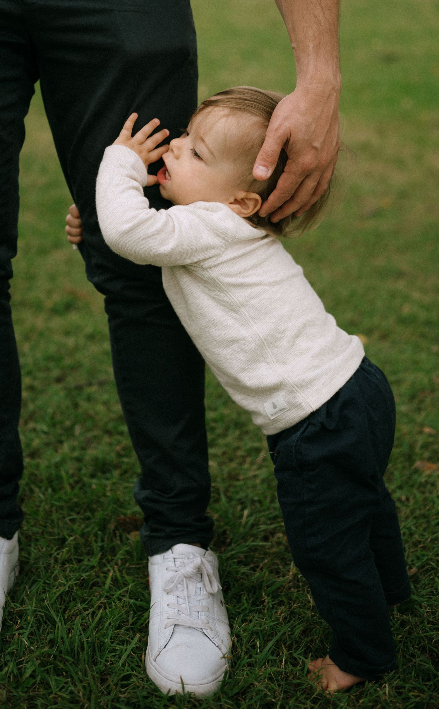 Close-up of small feet in white shoes walking on grass with adult guidance.