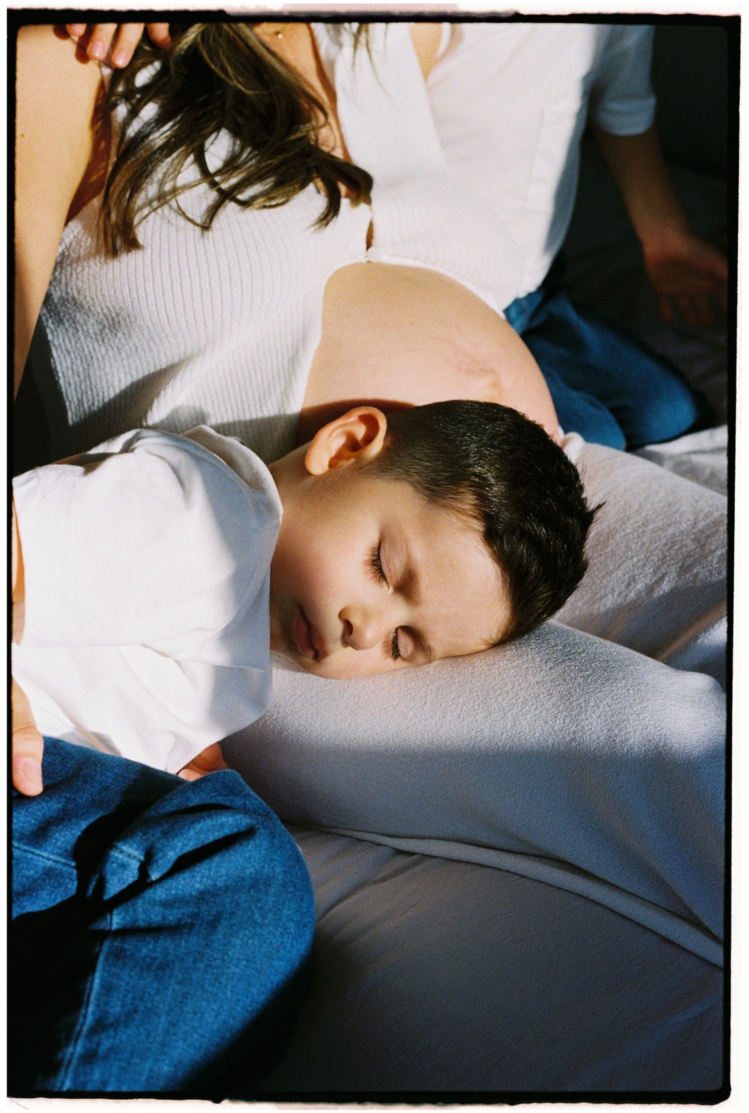 Child sleeping peacefully on white bedding in natural light.