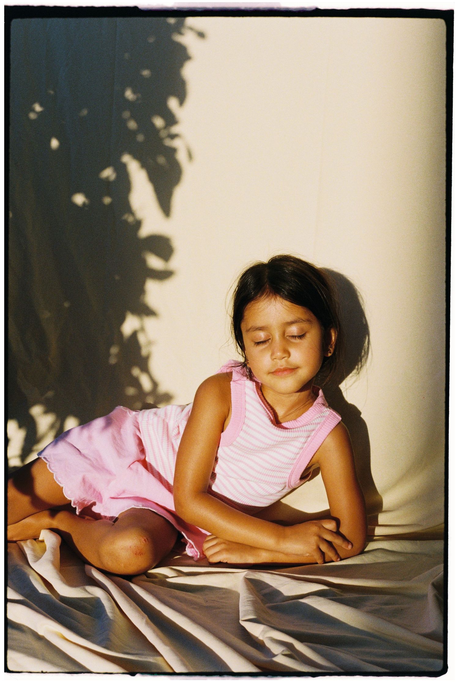 Dreamy portrait of young girl in pink striped dress resting on white sheets.