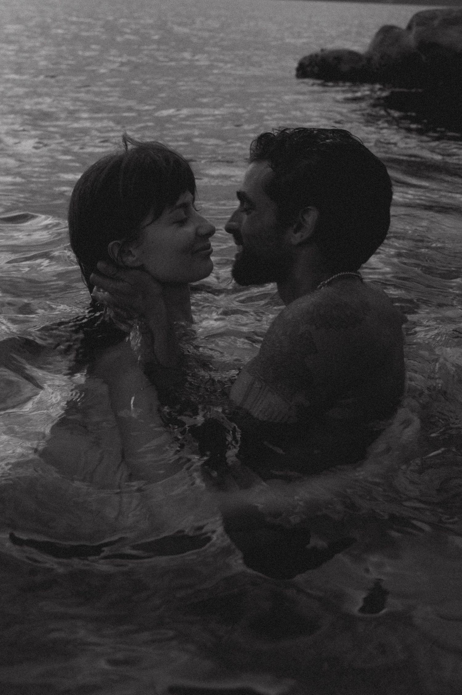 A couple shares an intimate moment while swimming in dark waters at dusk.