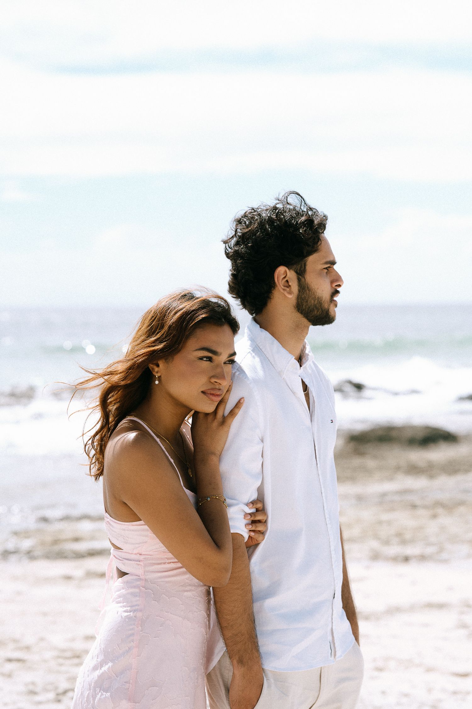 A couple in white clothing shares a joyful moment together on a sunny beach.