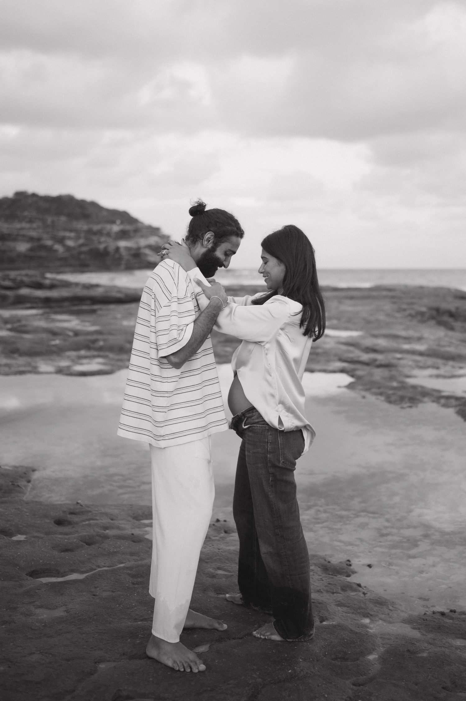 Two people in casual attire having a fun interaction on rocky coastal terrain.