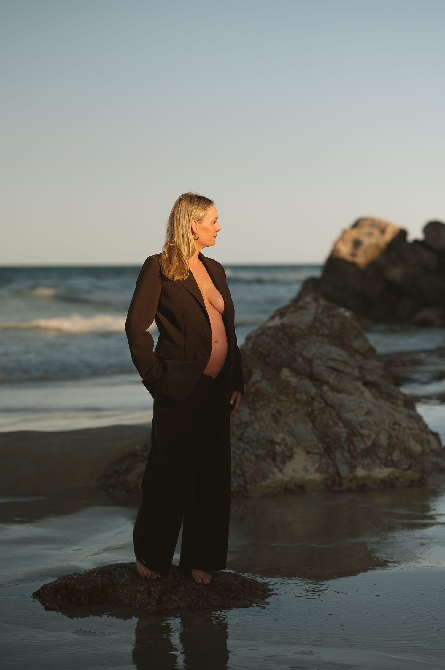 Silhouette of person in dark clothing against rocky beach at dusk.