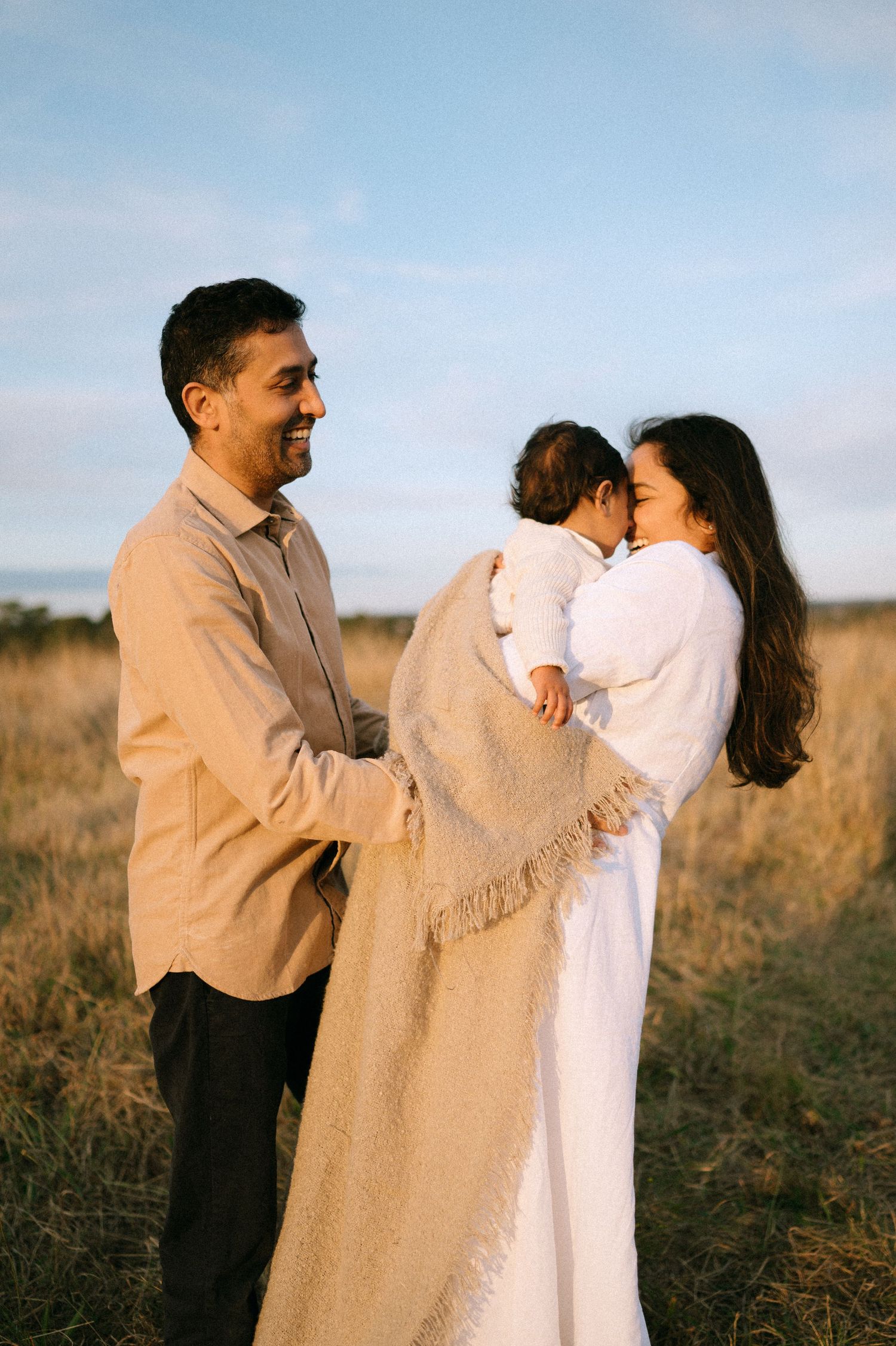 Family shares tender moment in field during golden hour.