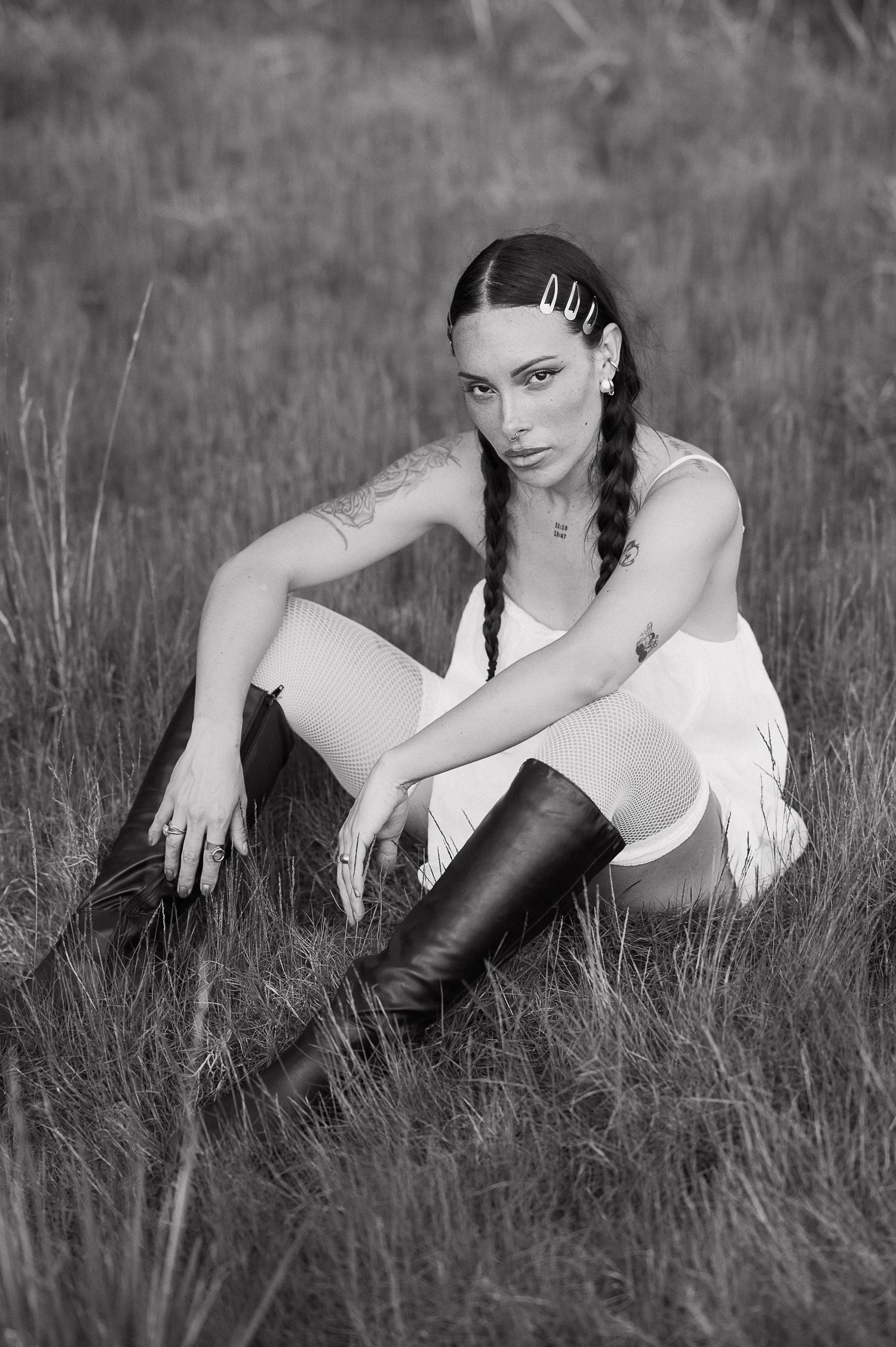 Black and white portrait in tall grass wearing white outfit and dark boots.
