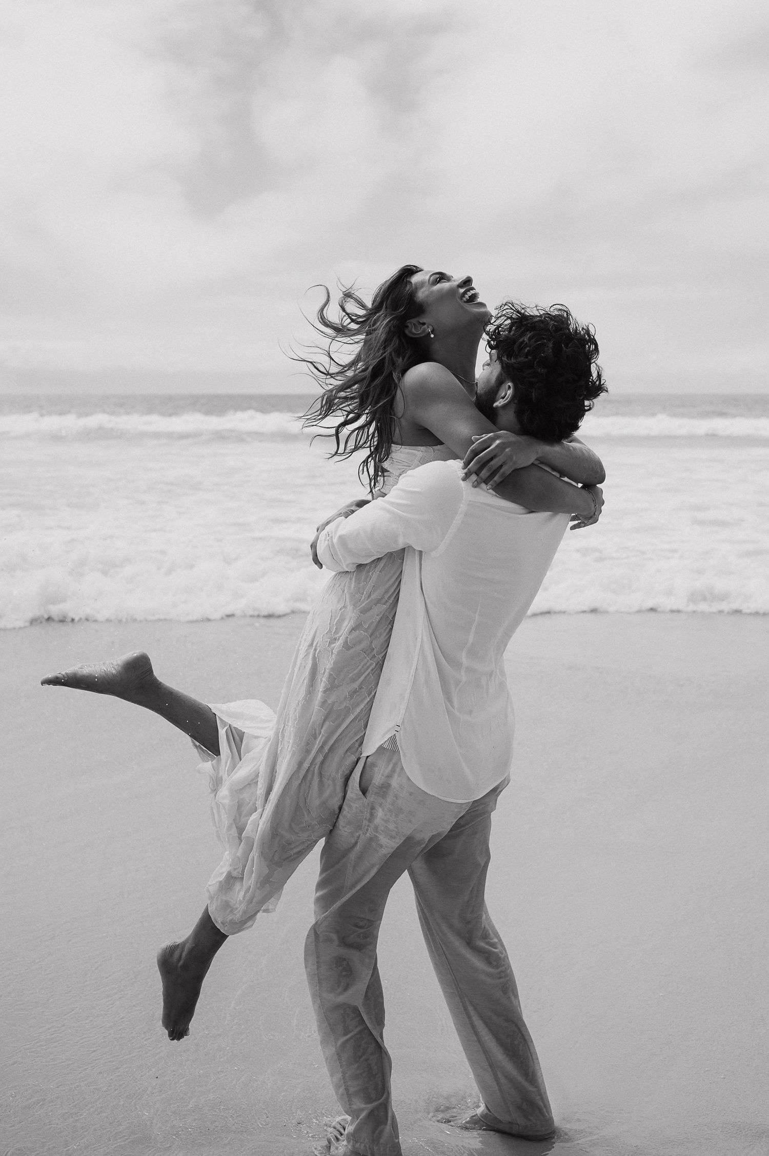 Couple in white clothing dancing together on a beach.