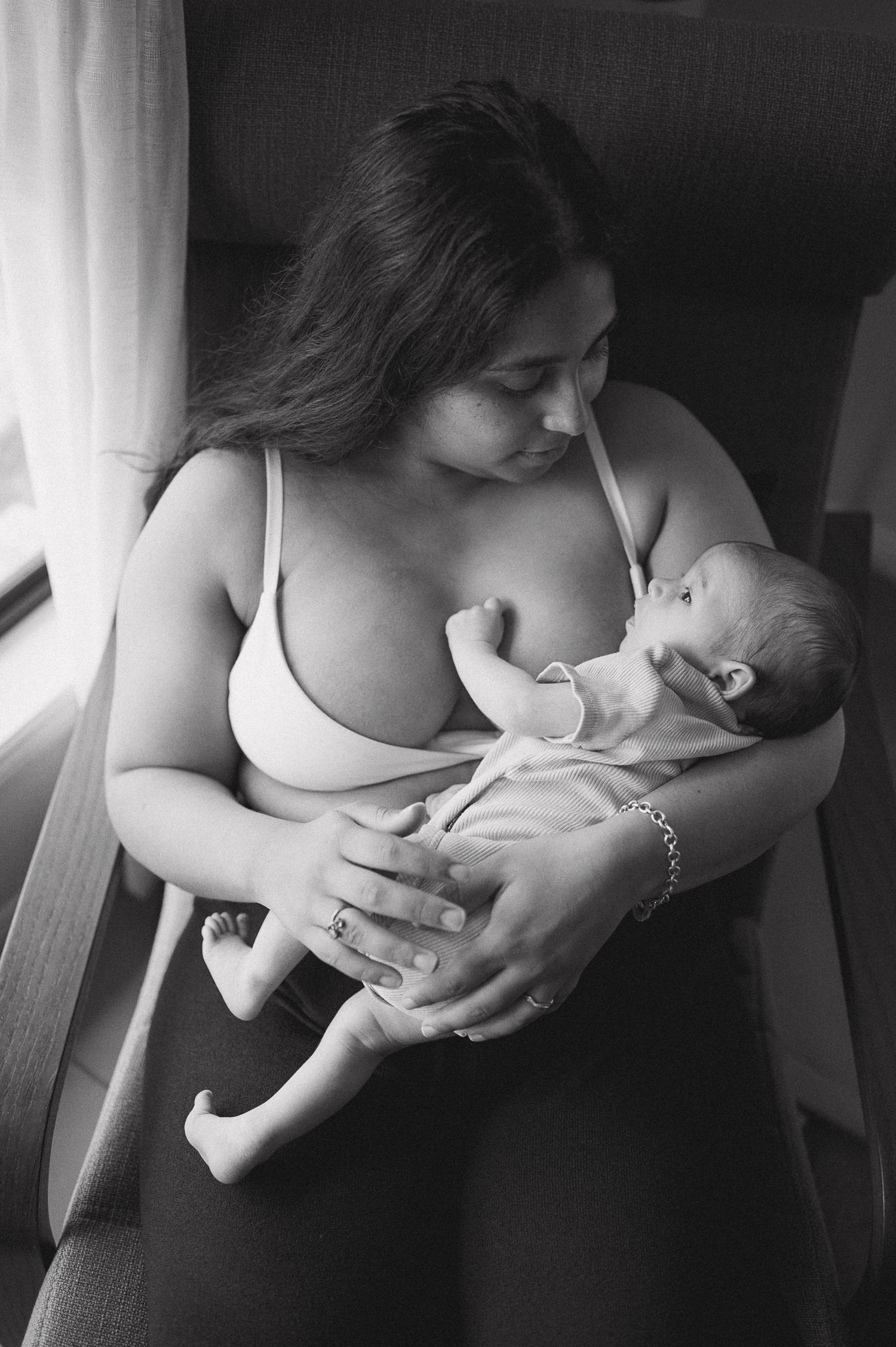 Black and white photo of a mother cradling her newborn baby while seated near a window.