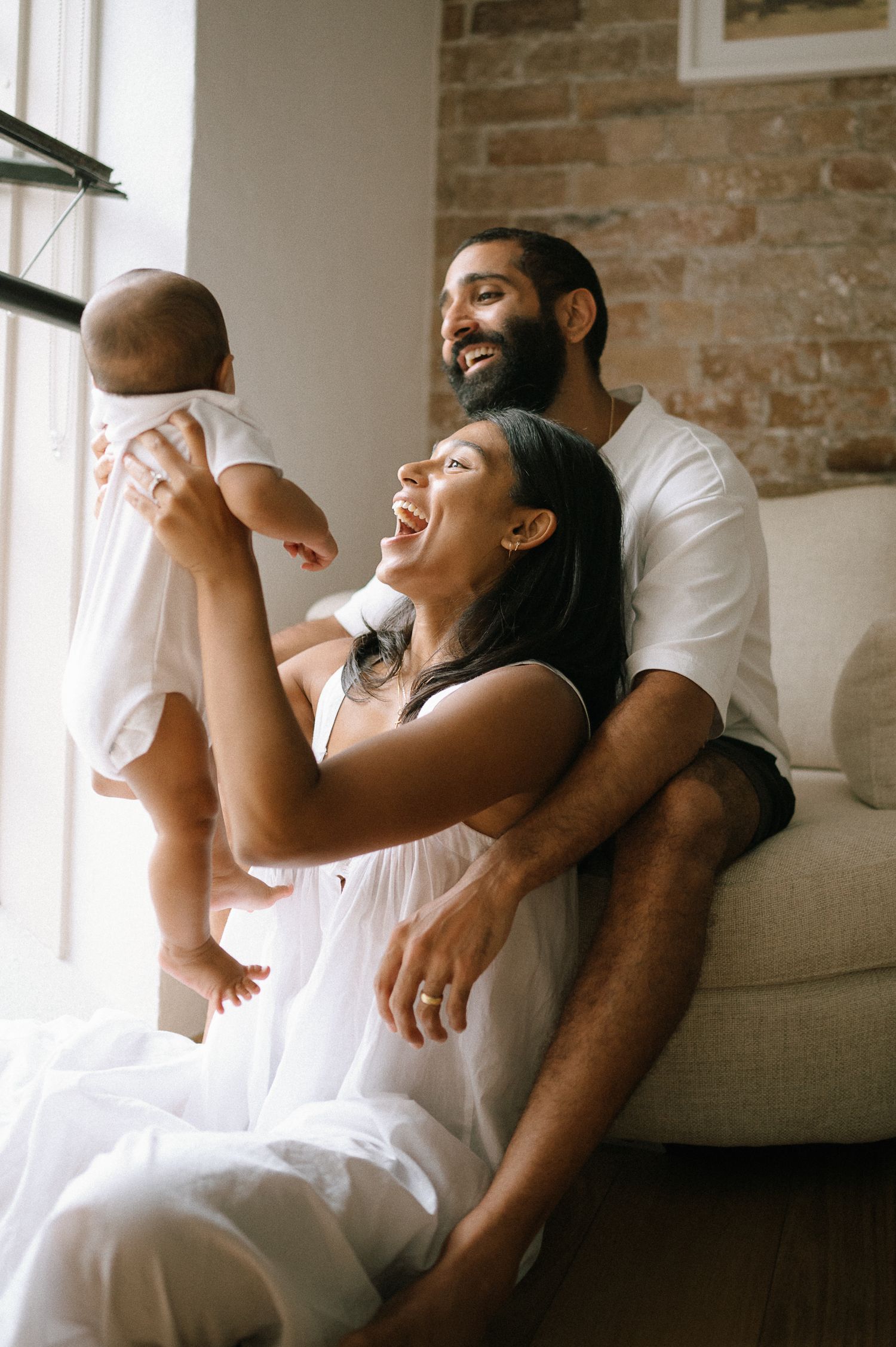 Couple in white clothing sharing joyful laughter during an indoor photoshoot.