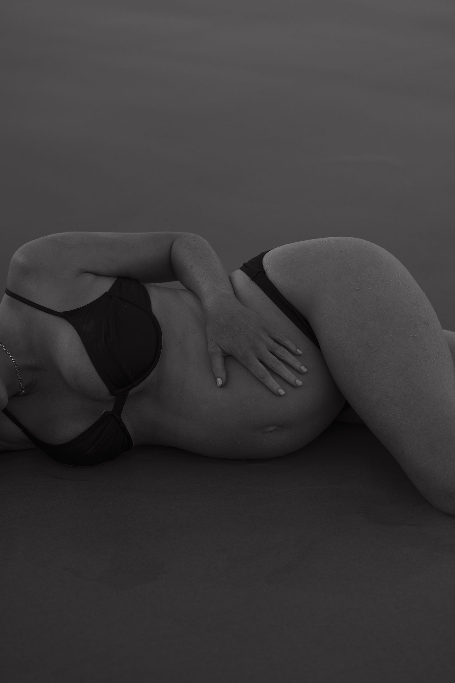 Artistic black and white nude maternity photo on dark background.