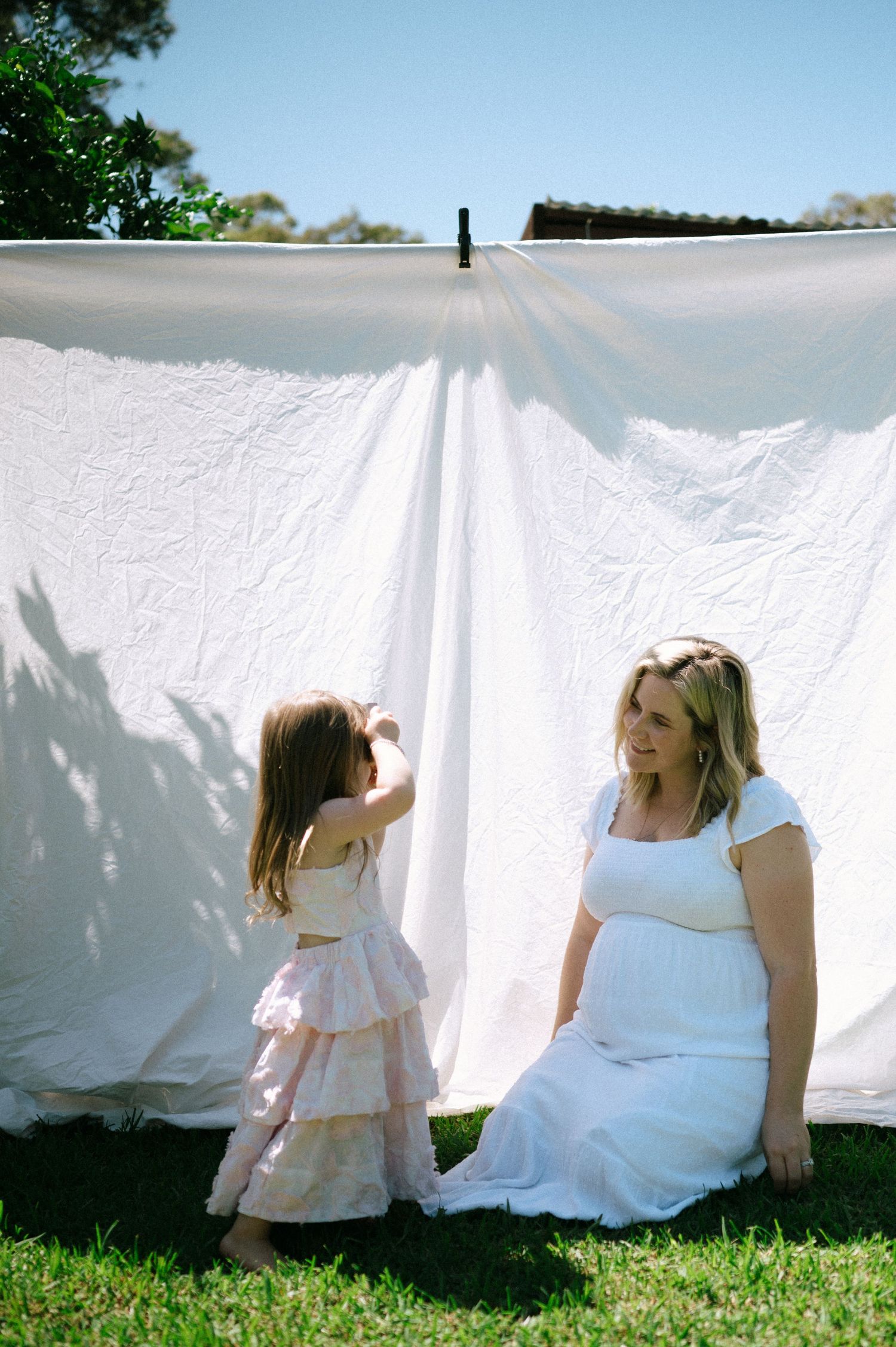 People playing peek-a-boo behind white sheets hanging on clothesline in backyard.